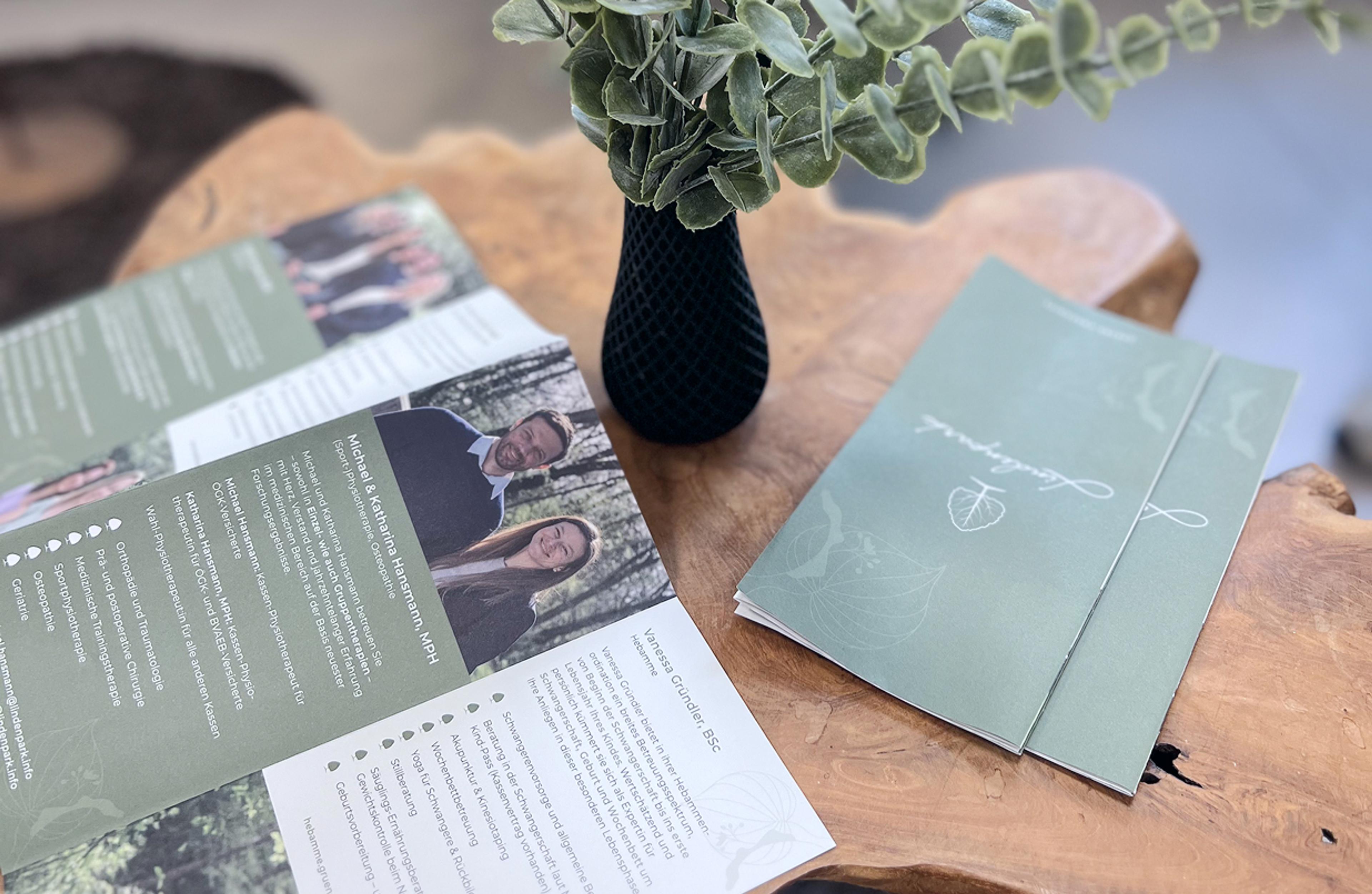 Physio Hansmann werden in der Lindenpark Broschüre vorgestellt – moderne grüne Broschüre mit Naturmotiven auf Holztisch. Branding für Lindenpark Gesundheitszentrum in Gössendorf bei Unerwartet Design Agentur.