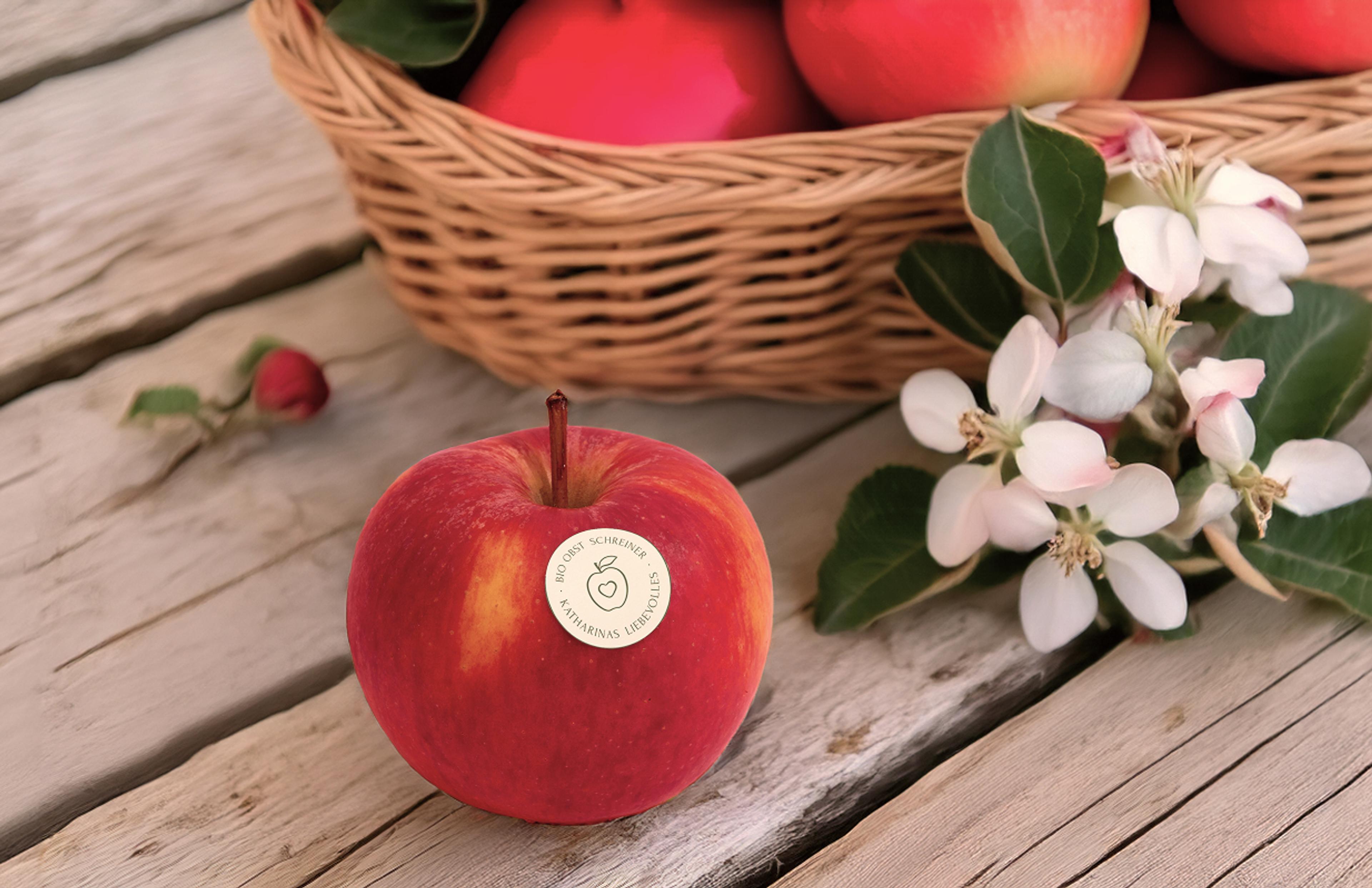 Roter Apfel mit dem Bio Obst Logo als Obststicker vor einem Apfelkorb verziert mit weißen Blumen.