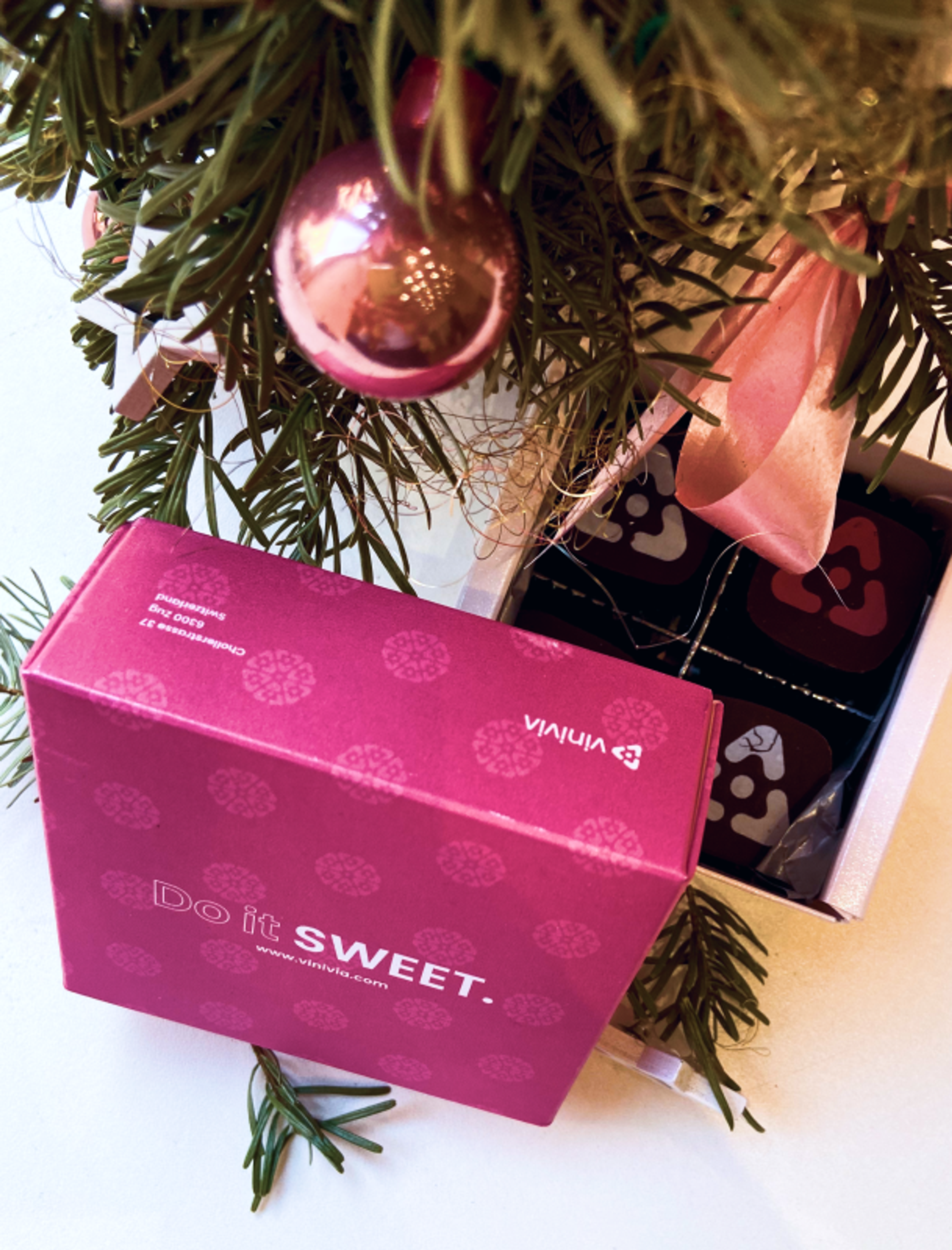 Geöffnete Vinivia-Geschenkbox mit detailreicher Verpackung und weihnachtlicher Dekoration, einschließlich pinker Christbaumkugeln – Unerwartet Design