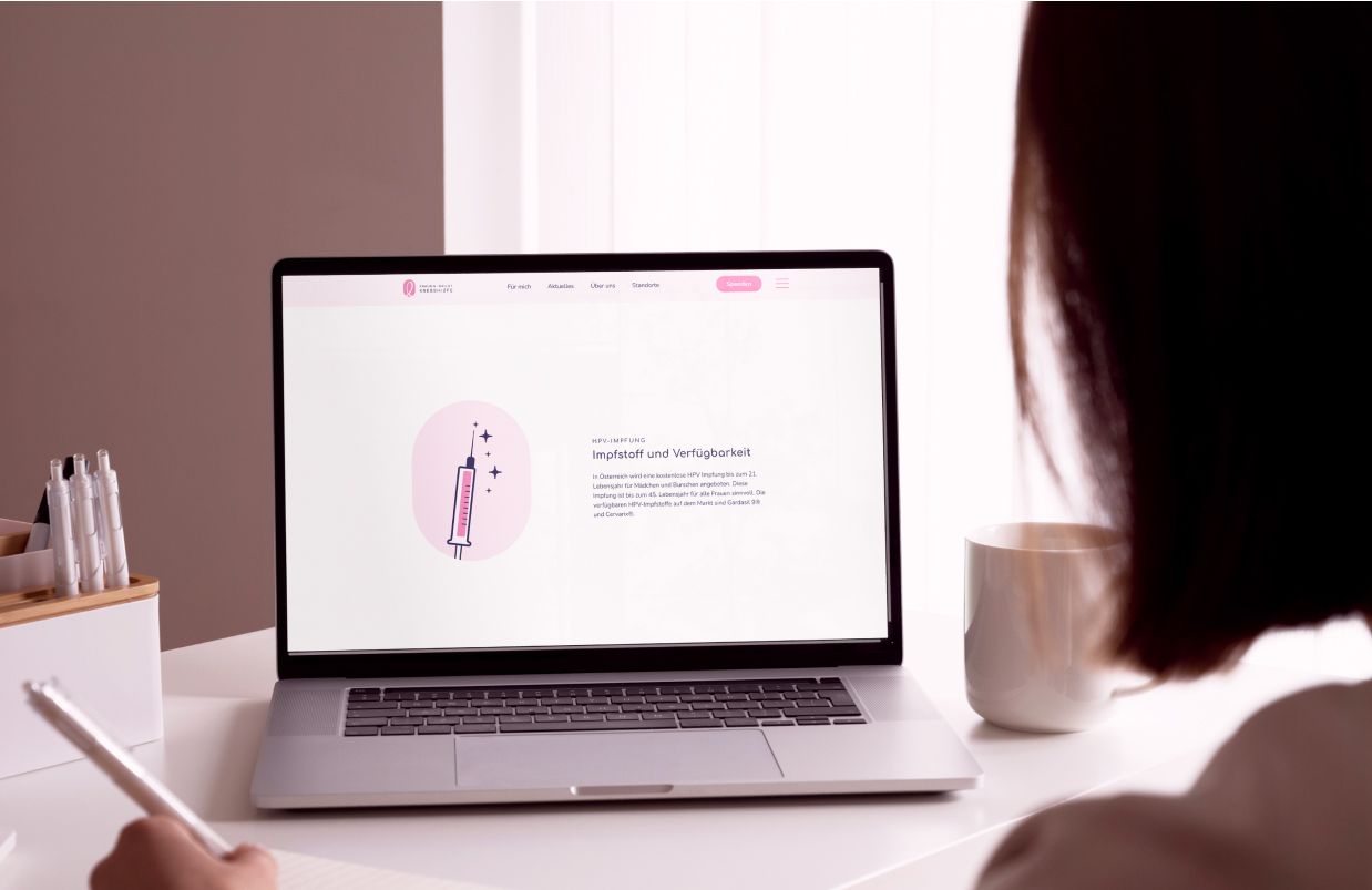 Ein Laptopbildschirm zeigt die HPV-Impfungsseite der Zauberfrauen-Website mit einer stilisierten Spritzen-Illustration. Die Seite bietet leicht verständliche Informationen zur Gesundheitsvorsorge und ist in einer klaren, minimalistischen Gestaltung gehalten.
