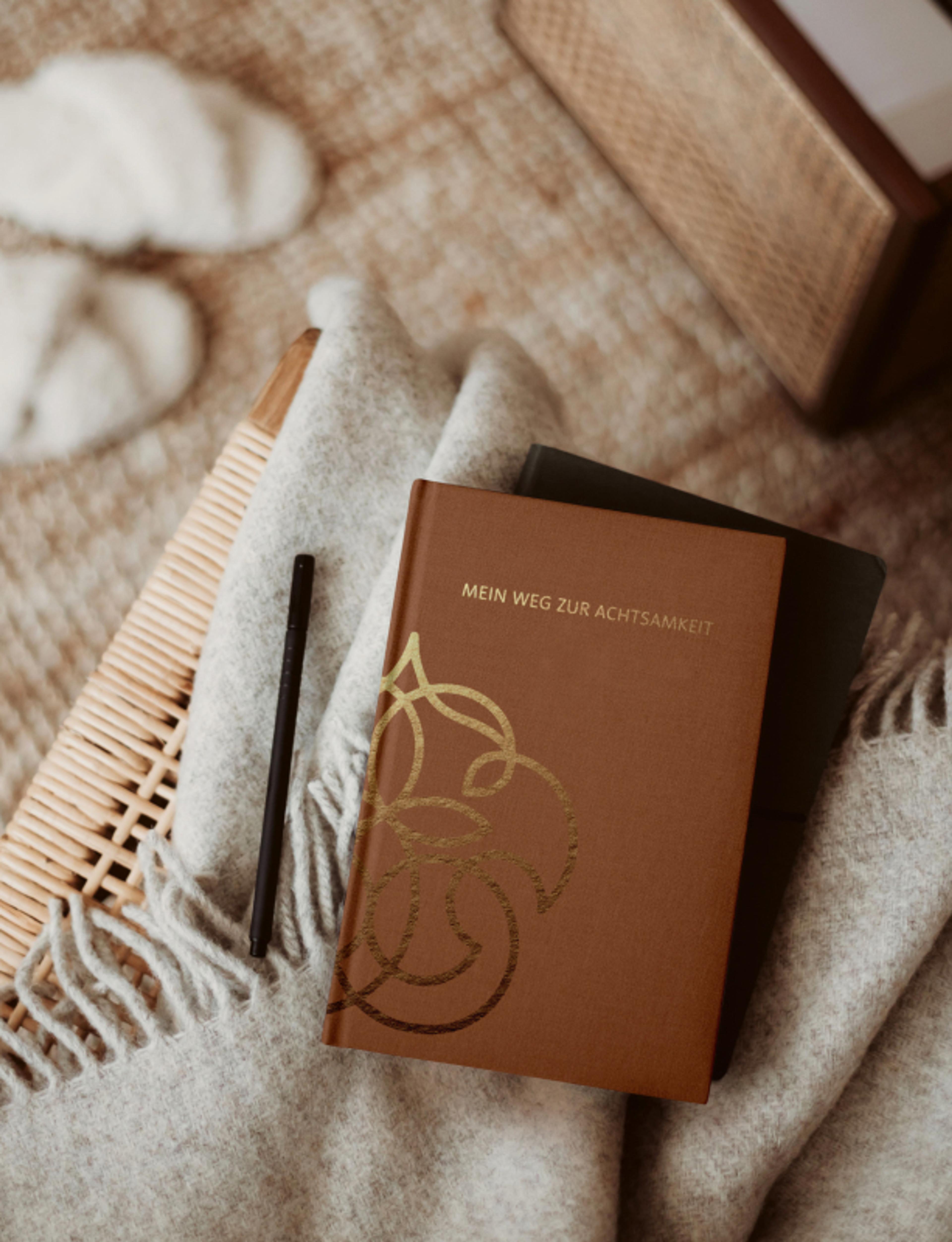 Hochwertiges Notizbuch mit geprägtem Logo von Kunter Bunter Weg, designed für Achtsamkeit und Coaching. Gestaltung von Unerwartet Design Graz.