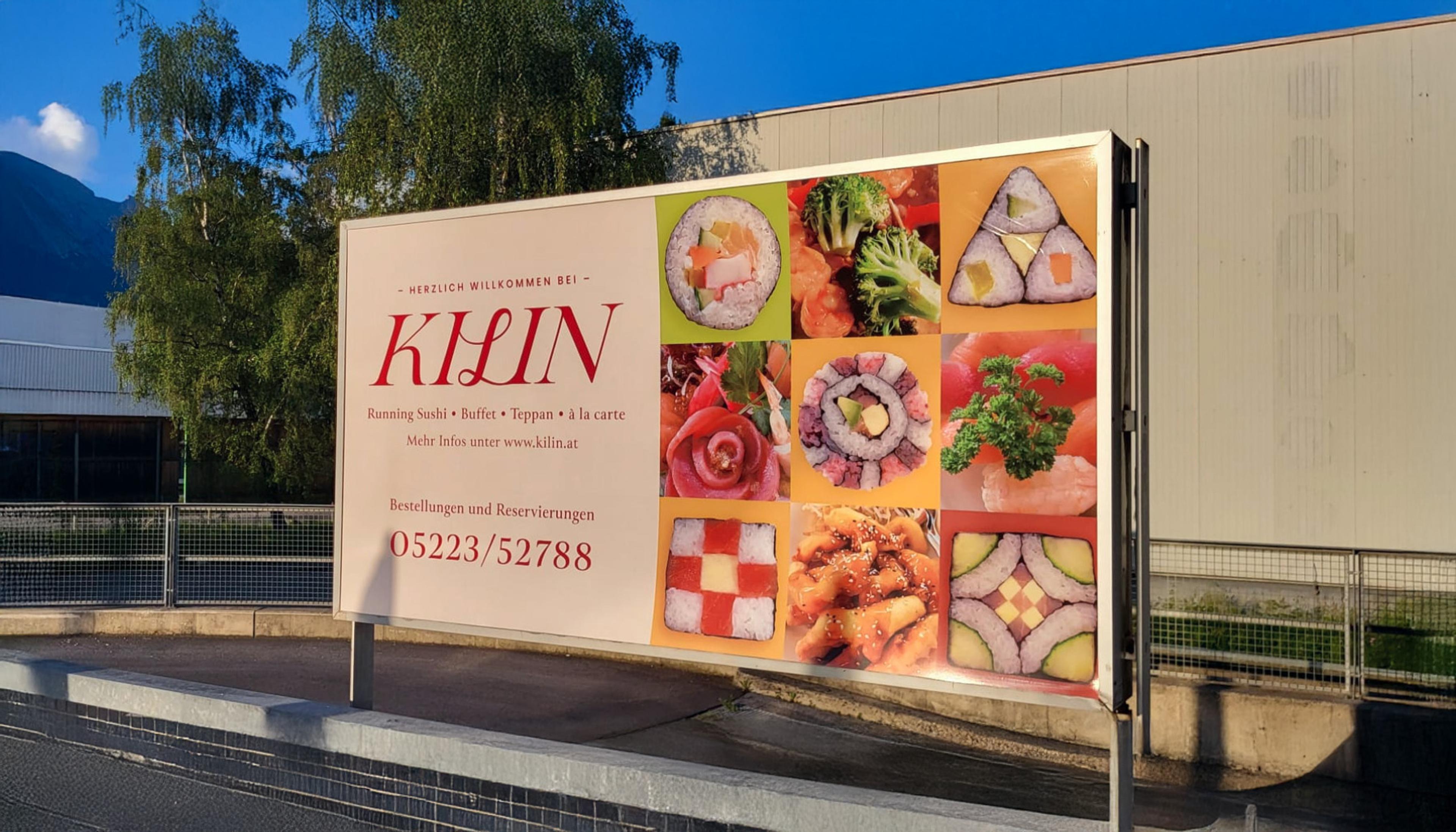 Große Werbetafel des Kilin Restaurants mit stilvollem Branding und asiatischem Design. Hochwertige Bilder von Sushi, Teppanyaki und kreativen Sushi-Kreationen ziehen die Aufmerksamkeit auf sich. Klare Typografie mit wichtigen Informationen zu Running Sushi, Buffet und Teppan-Grill, inklusive Telefonnummer für Reservierungen. Perfekte Außenwerbung für asiatische Gastronomie, umgesetzt von Unerwartet Branding und Design OG aus Graz, Österreich.