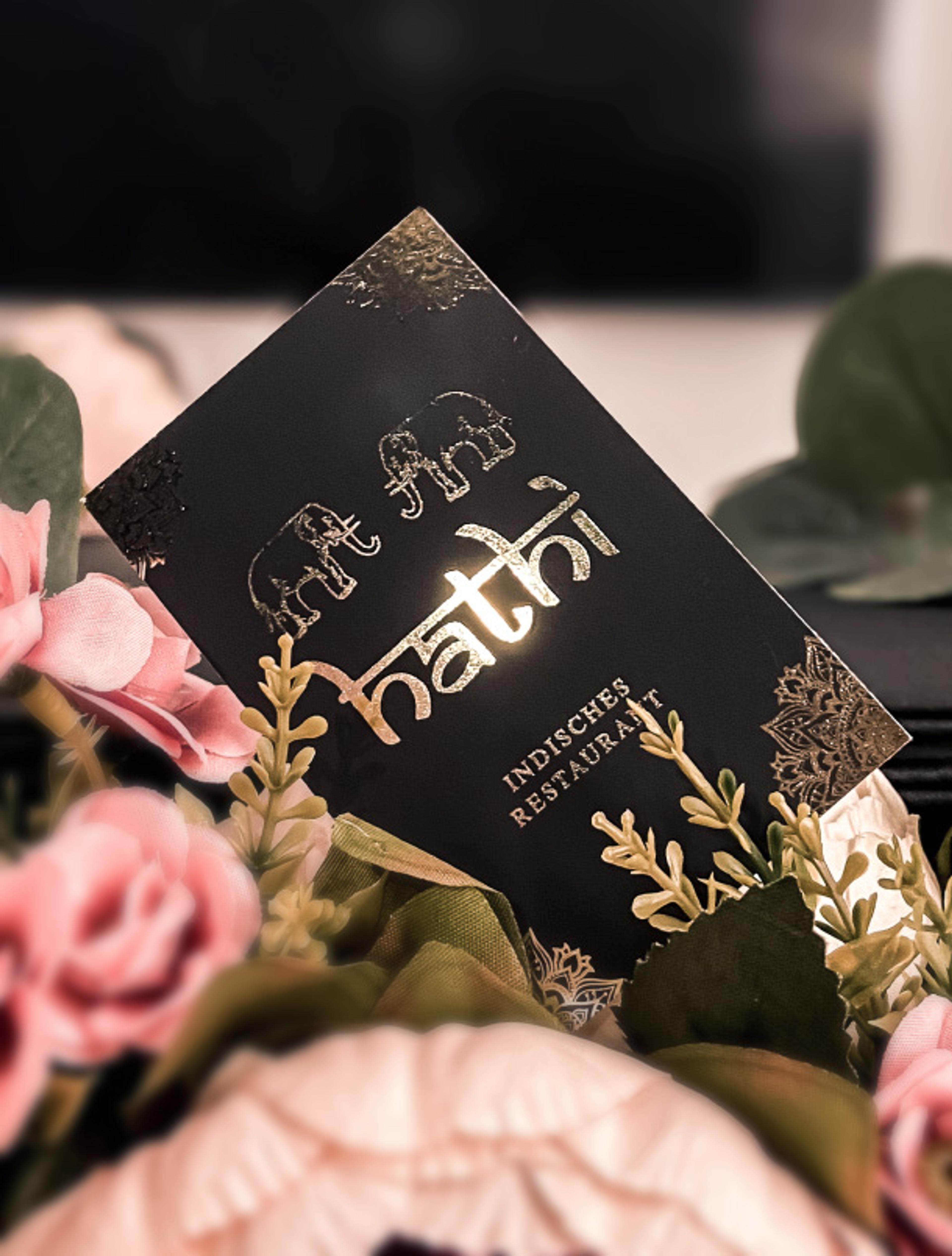 Hochwertiges Corporate Design für das Hathi indische Restaurant mit einer kunstvoll gestalteten Speisekarte und Visitenkarte. Goldene Mandala-Muster und Elefantenlogos auf tiefschwarzem Hintergrund vermitteln Exklusivität und Authentizität. Edles Gastronomie-Branding, entwickelt von Unerwartet Branding und Design OG aus Graz, Österreich.