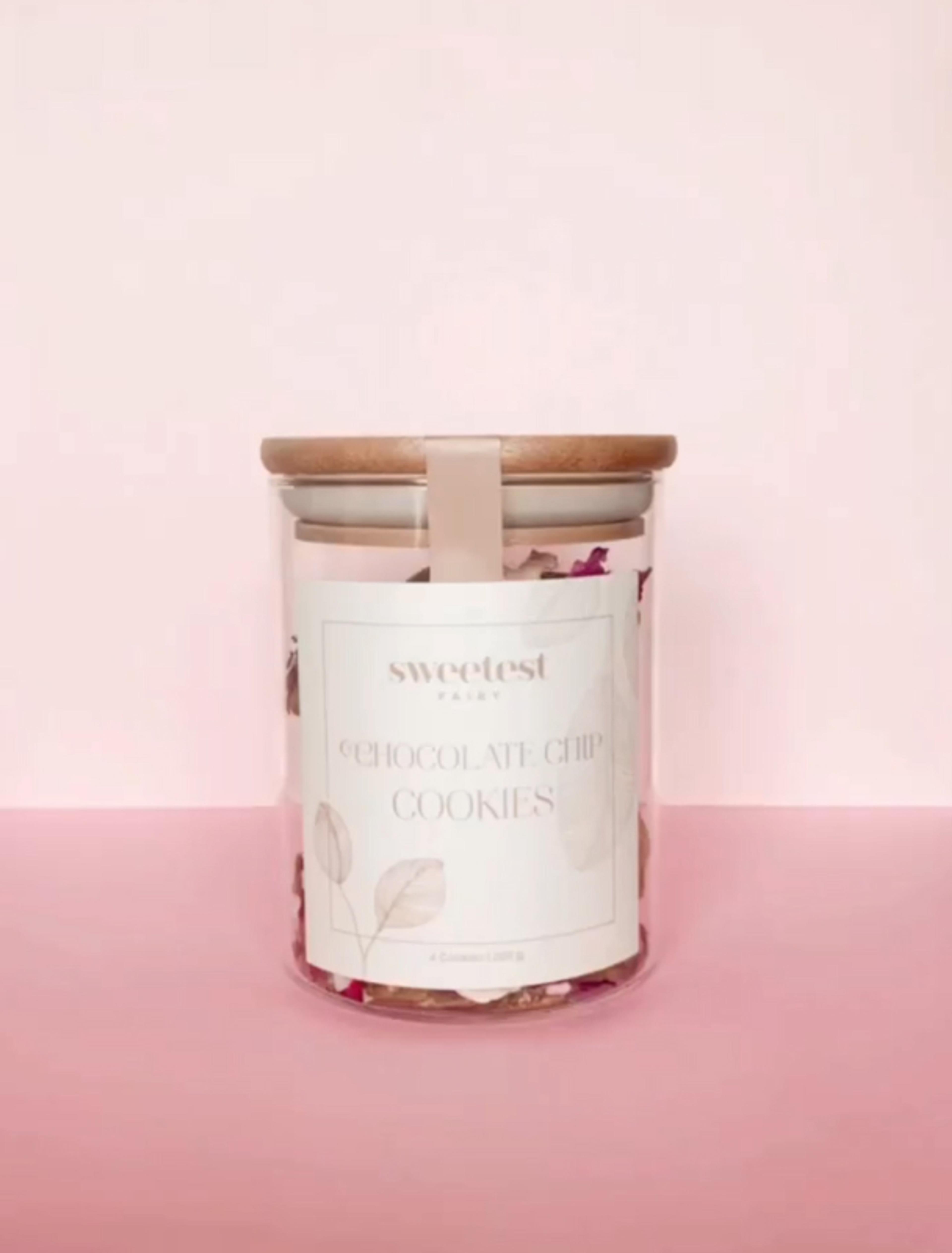 Sweetest Fairy | Sarah Frost Premium-Verpackung für handgemachte Schokoladenkekse in einer edlen Glasverpackung mit Holzdeckel. Hochwertiges Design mit eleganter Typografie und natürlicher Farbpalette, perfekt für Luxus-Feinkost, Geschenkboxen und exklusive Bäckereiprodukte. Nachhaltige Verpackungslösung für Unternehmen mit Fokus auf stilvolles Branding. Konzept von Unerwartet Branding und Design OG aus Graz, Österreich.