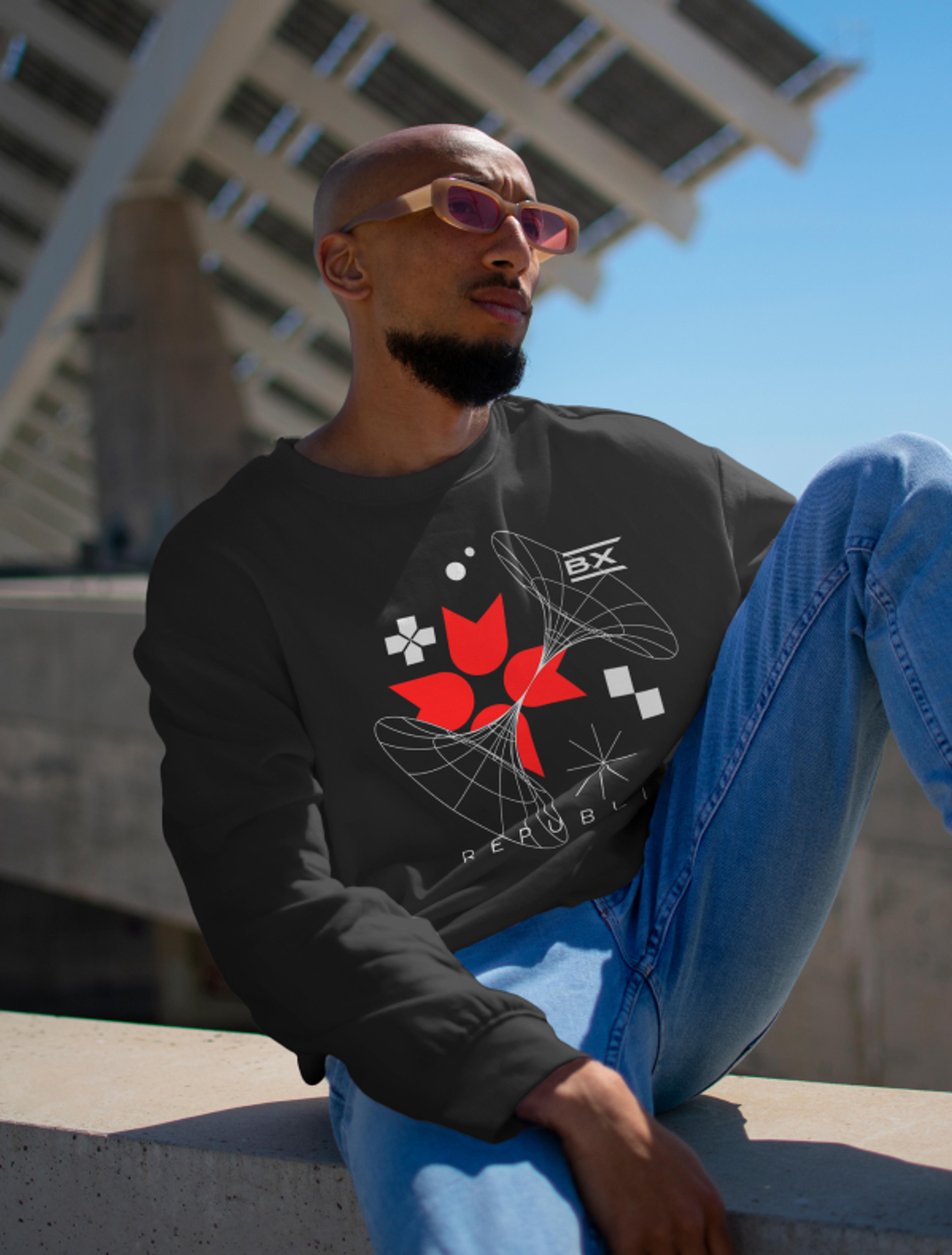 Mann mit modernem schwarzen Sweater mit abstraktem Grafikdesign und Bazix-Branding, lässig sitzend in urbaner Umgebung.