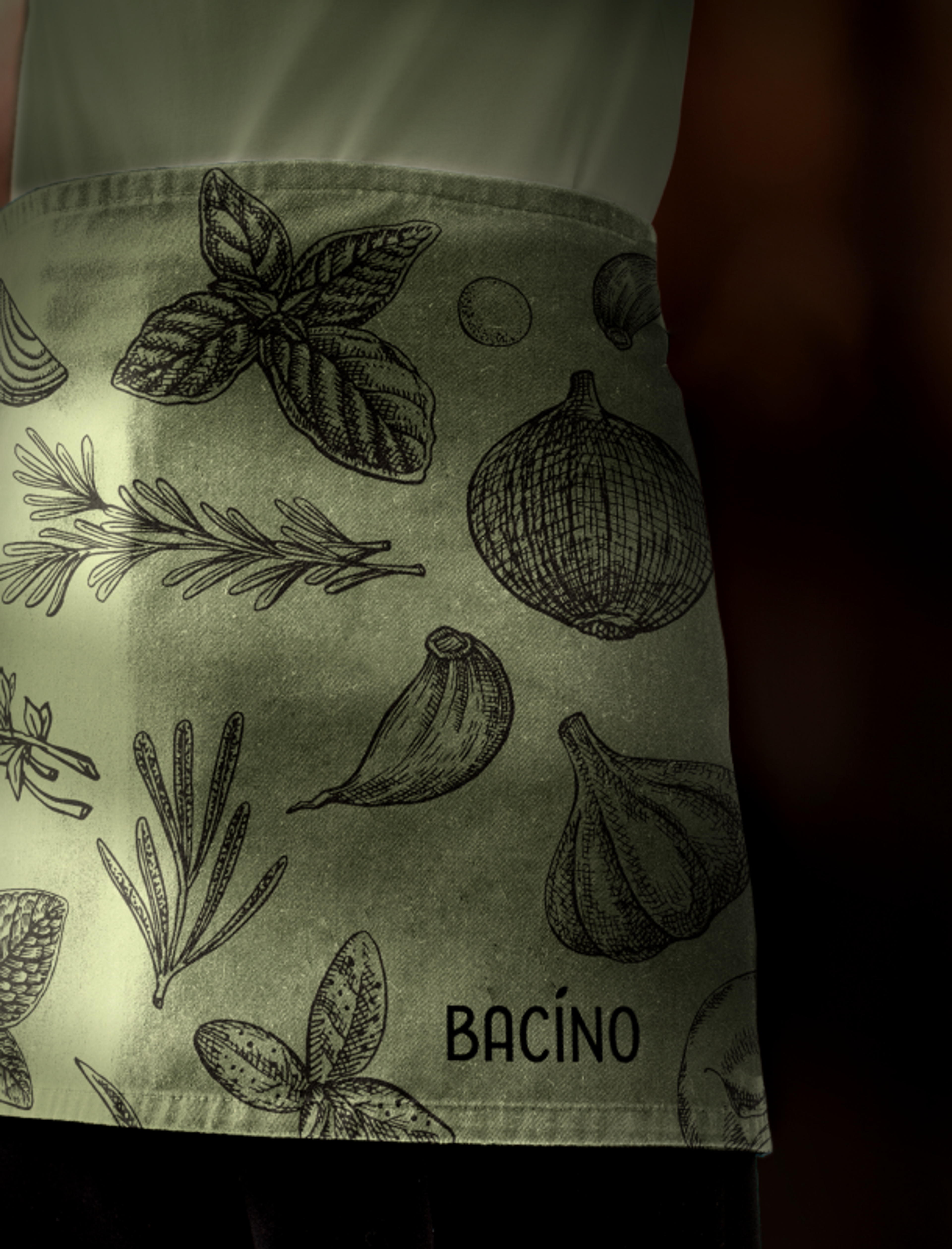 Kochschürze von Bacino mit handgezeichneten mediterranen Kräuterillustrationen und dem Bacino-Logo.