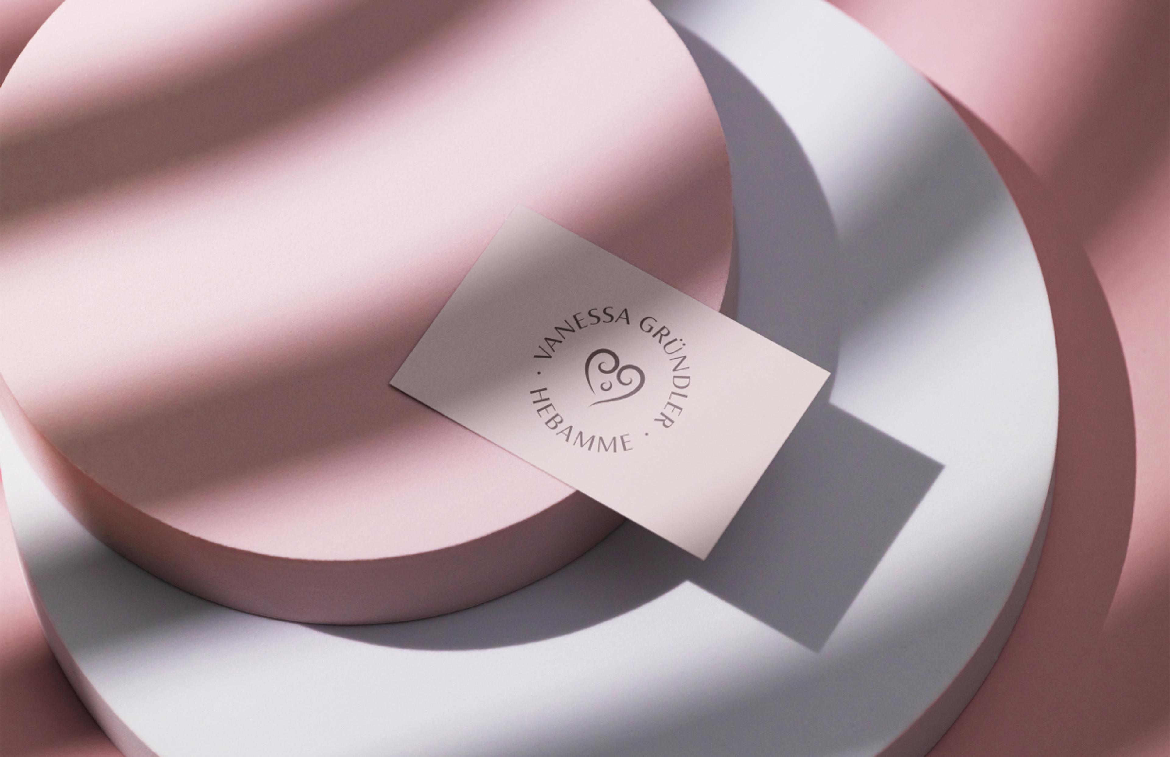 Visitenkarte von Hebamme Vanessa Gründler auf sanftem Rosa. Das Herz-Logo symbolisiert Fürsorge und Nähe, während die elegante Serifenschrift Vertrauen und Kompetenz ausstrahlt.