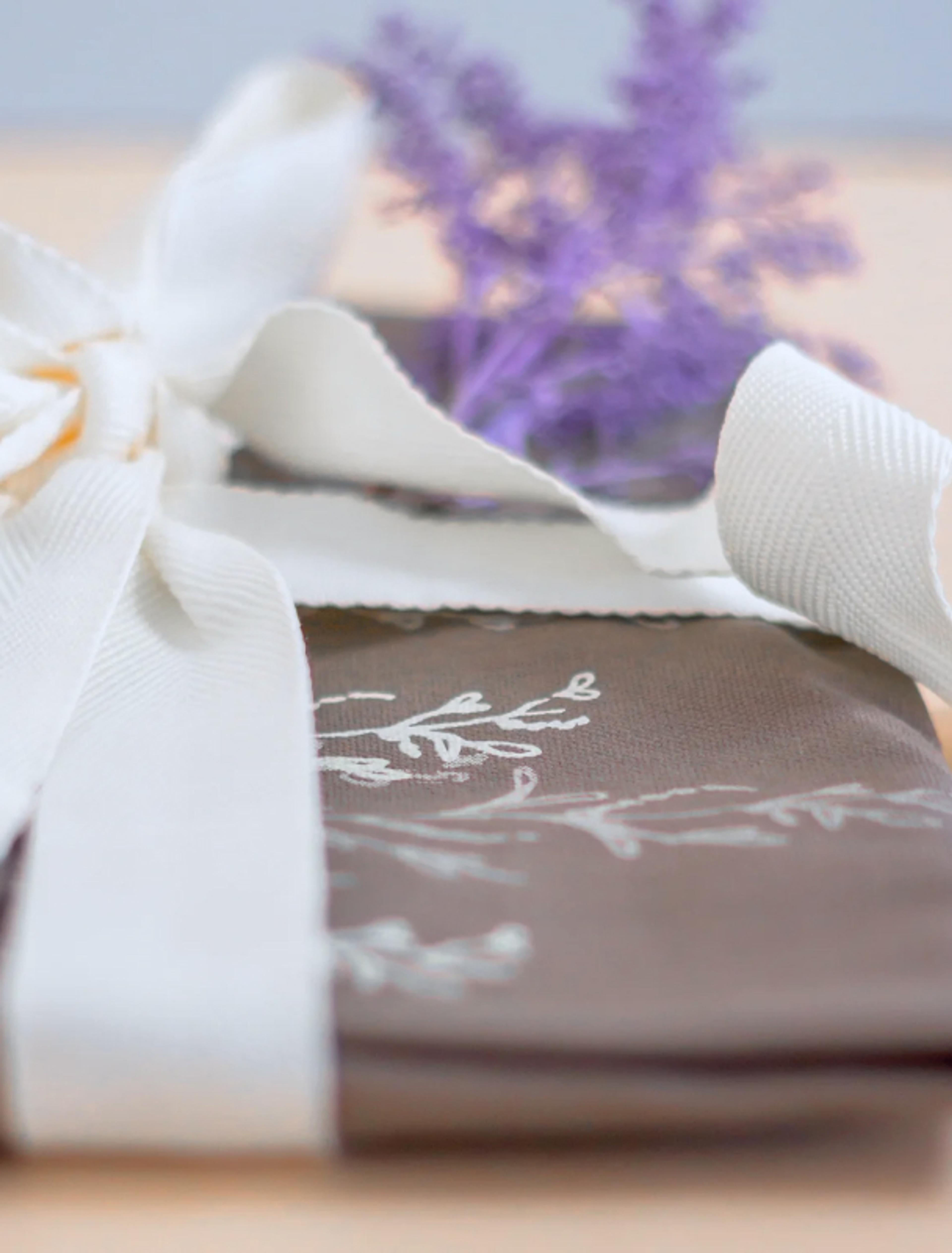 Sweetest Fairy | Sarah Frost Ganzheitliches Markenkonzept für Sweetest Fairy, das Handarbeit, Hochwertigkeit und Nachhaltigkeit vereint. Von der Logoentwicklung bis zur Verpackung – ein durchdachtes Branding von Unerwartet Design in Graz für eine neuseeländische Patisserie. Das Bild zeigt eine Schürze - liebvoll verpackt mit einer Masche. Lavendel im Hintergrund.