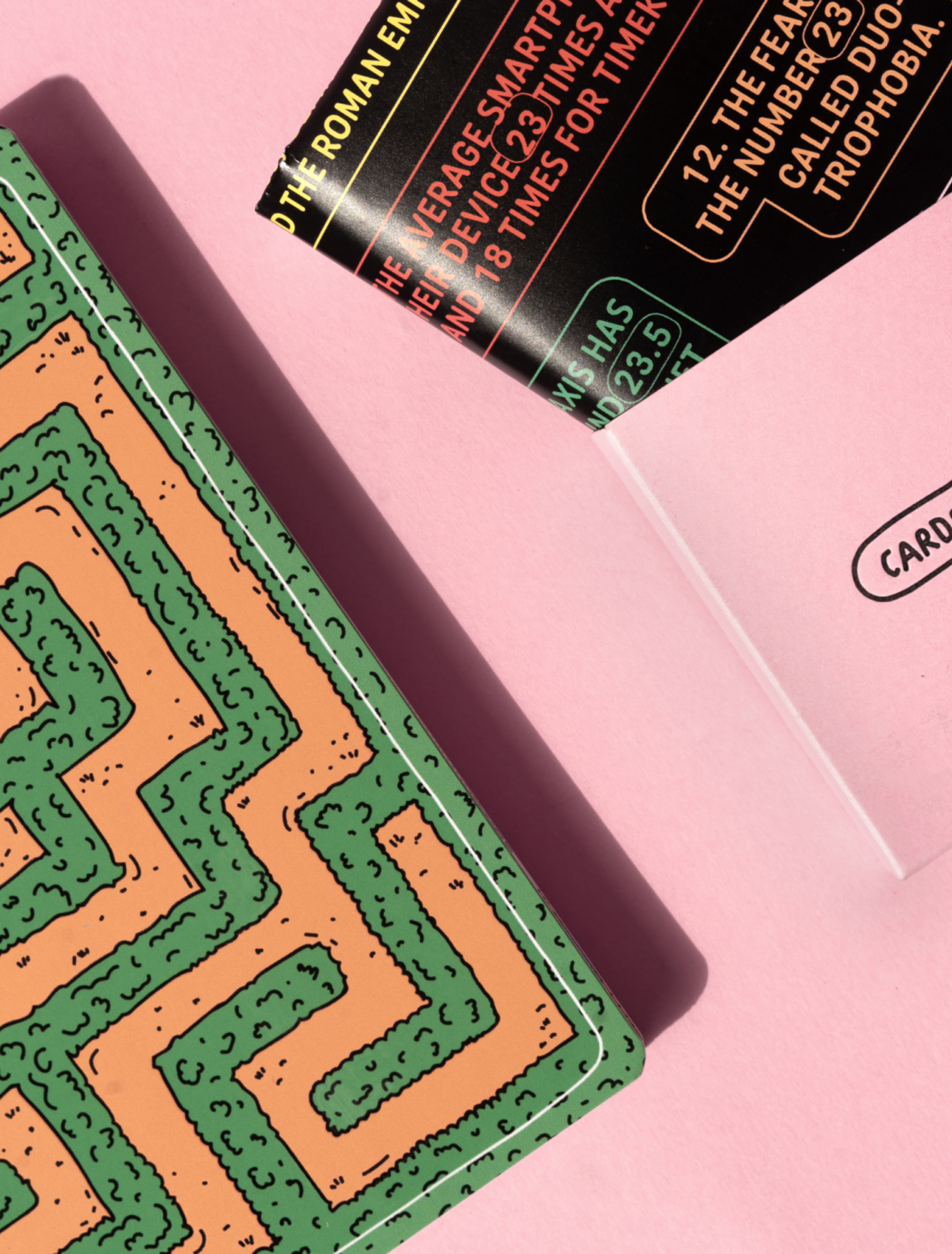 Miriam Leitinger Kartenset „Cards for Procrastination“ mit einem grünen Labyrinth-Design auf rosa Hintergrund. Eine Karte mit Fun-Facts ragt aus einem Umschlag mit dem Logo.