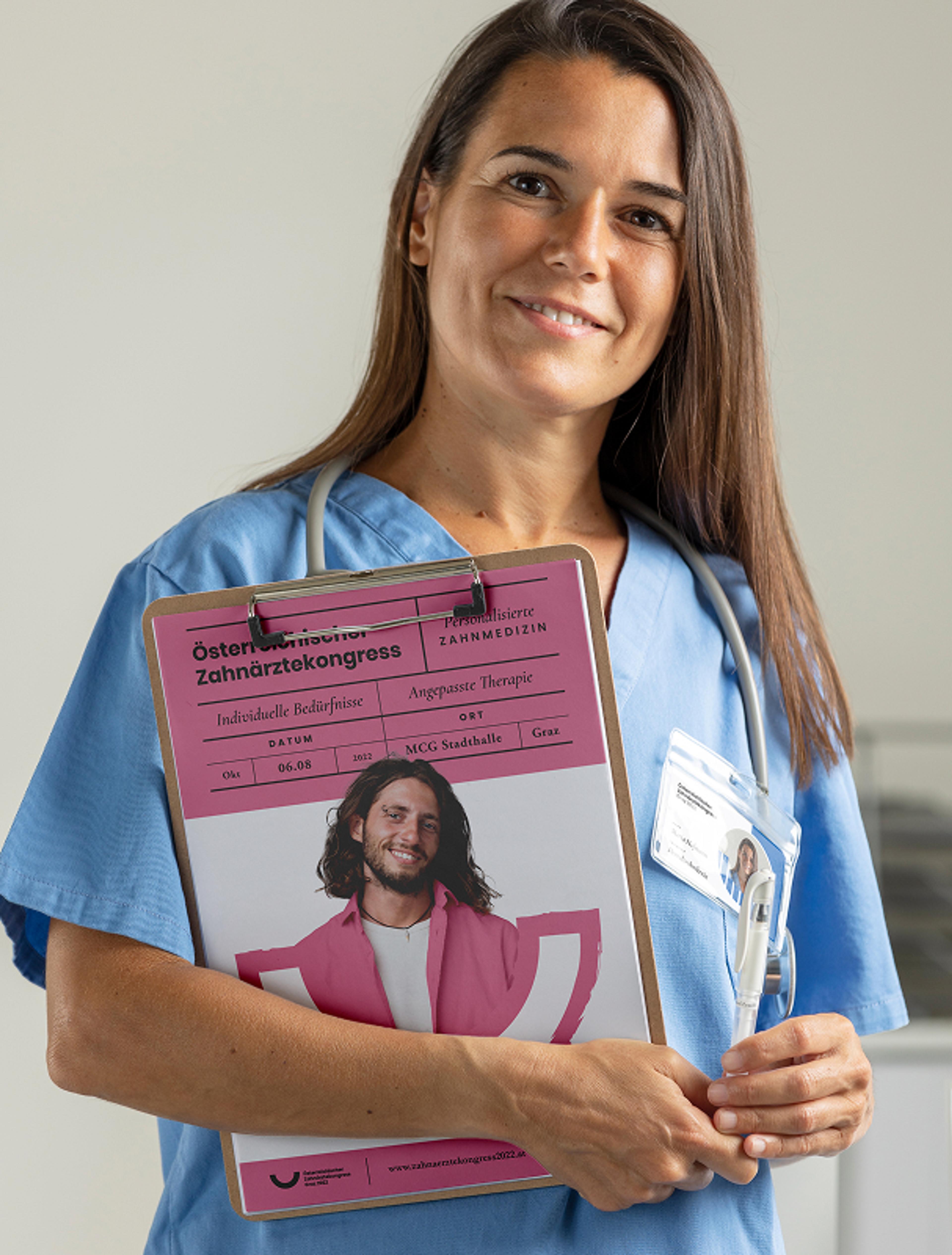 Ärztin in blauer Berufskleidung hält ein pinkes Klemmbrett mit einem Plakat des Österreichischen Zahnärztekongresses Graz 2022, entworfen von Unverwartet Design.