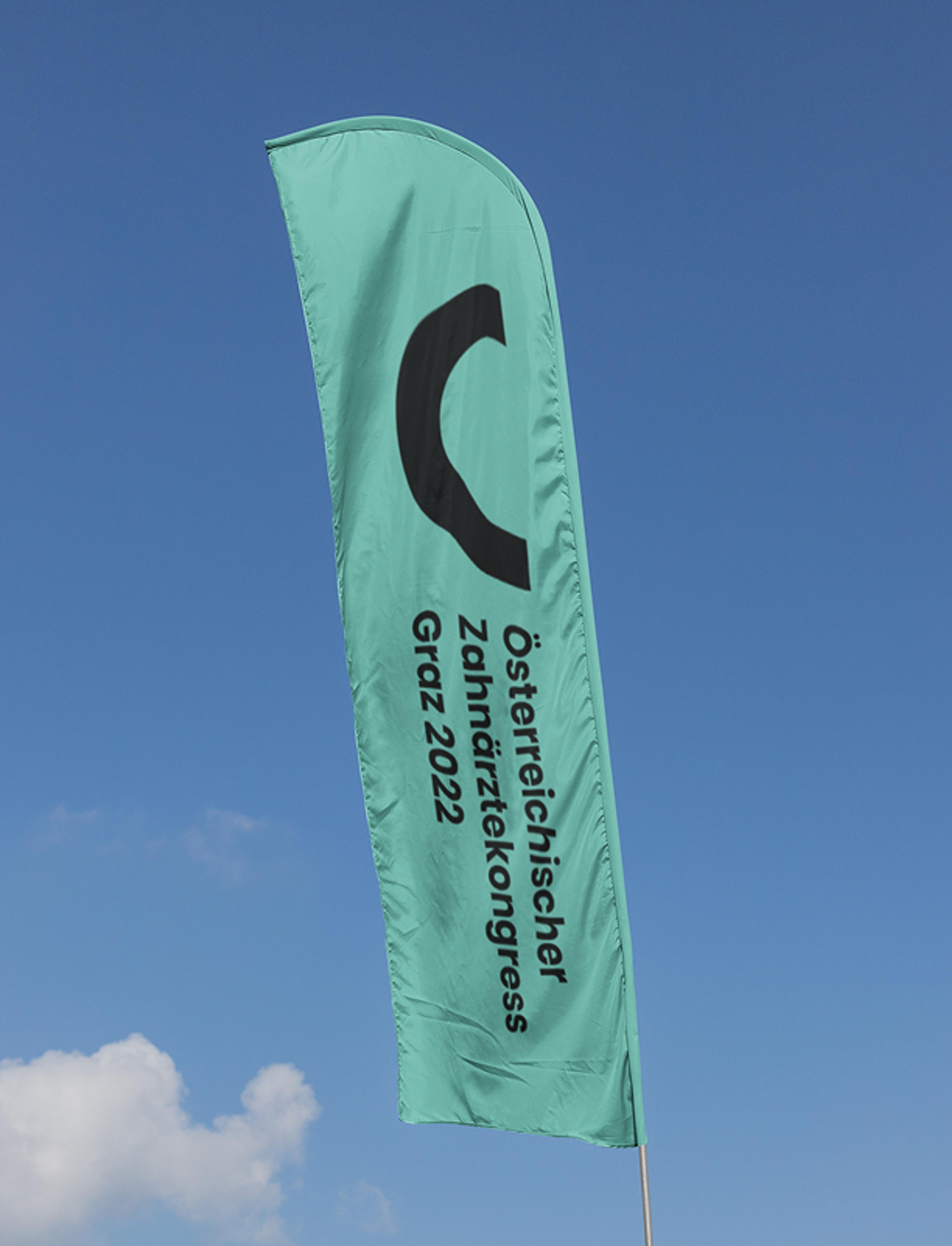 Grüne Fahne mit dem Logo des Österreichischen Zahnärztekongresses Graz 2022, flatternd vor blauem Himmel. Modernes Corporate Design von Unverwartet Design.