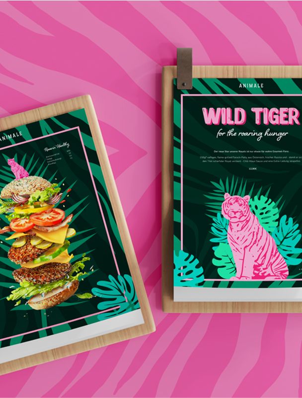 Zwei Speisekarten des Restaurants Animale auf Holzunterlagen mit tropischem Design, eine zeigt einen gestapelten Burger, die andere einen pinken Tiger mit dem Schriftzug „Wild Tiger“.