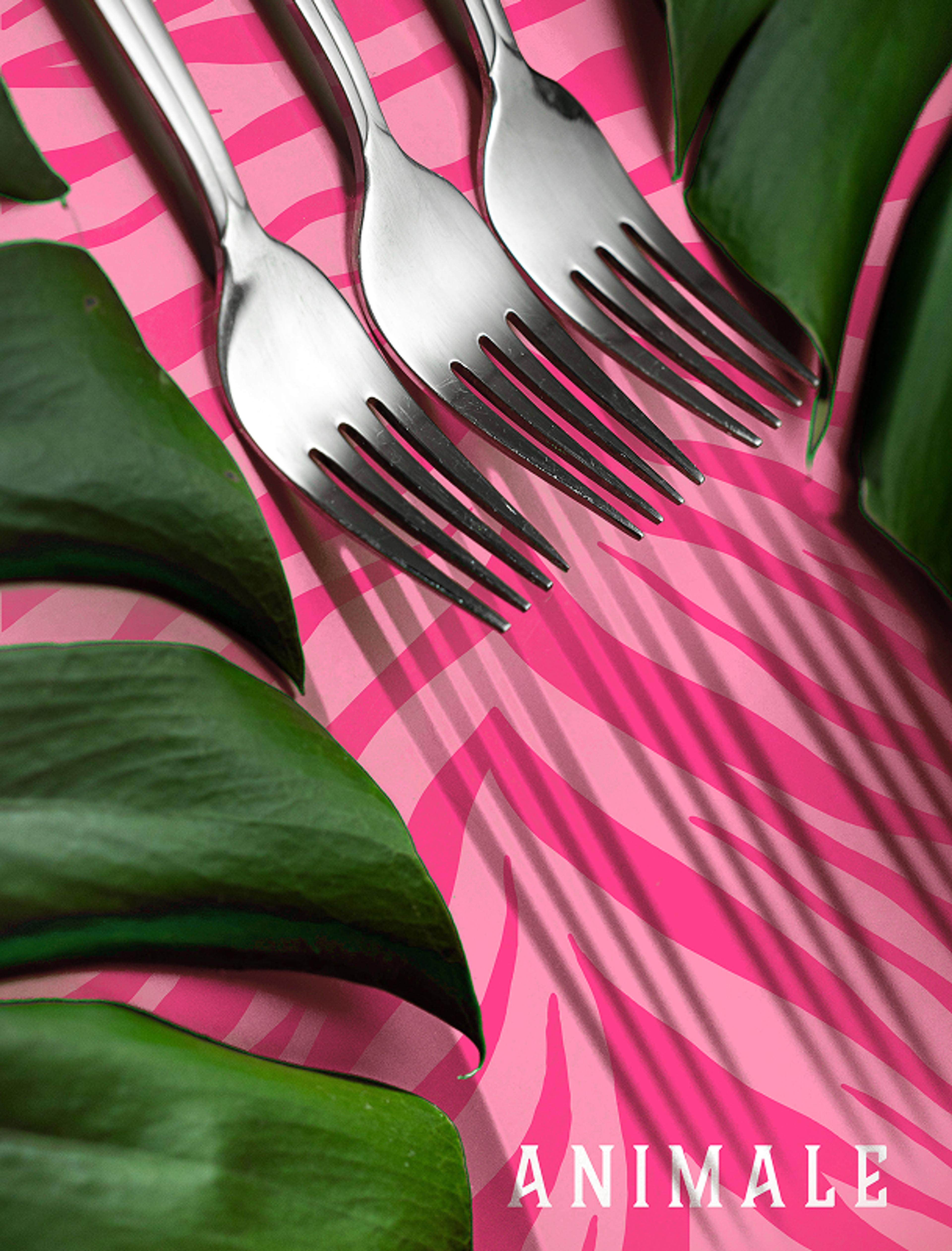 Drei silberne Gabeln auf einer Tischdecke mit pinkem Zebramuster, umrahmt von grünen Blättern.