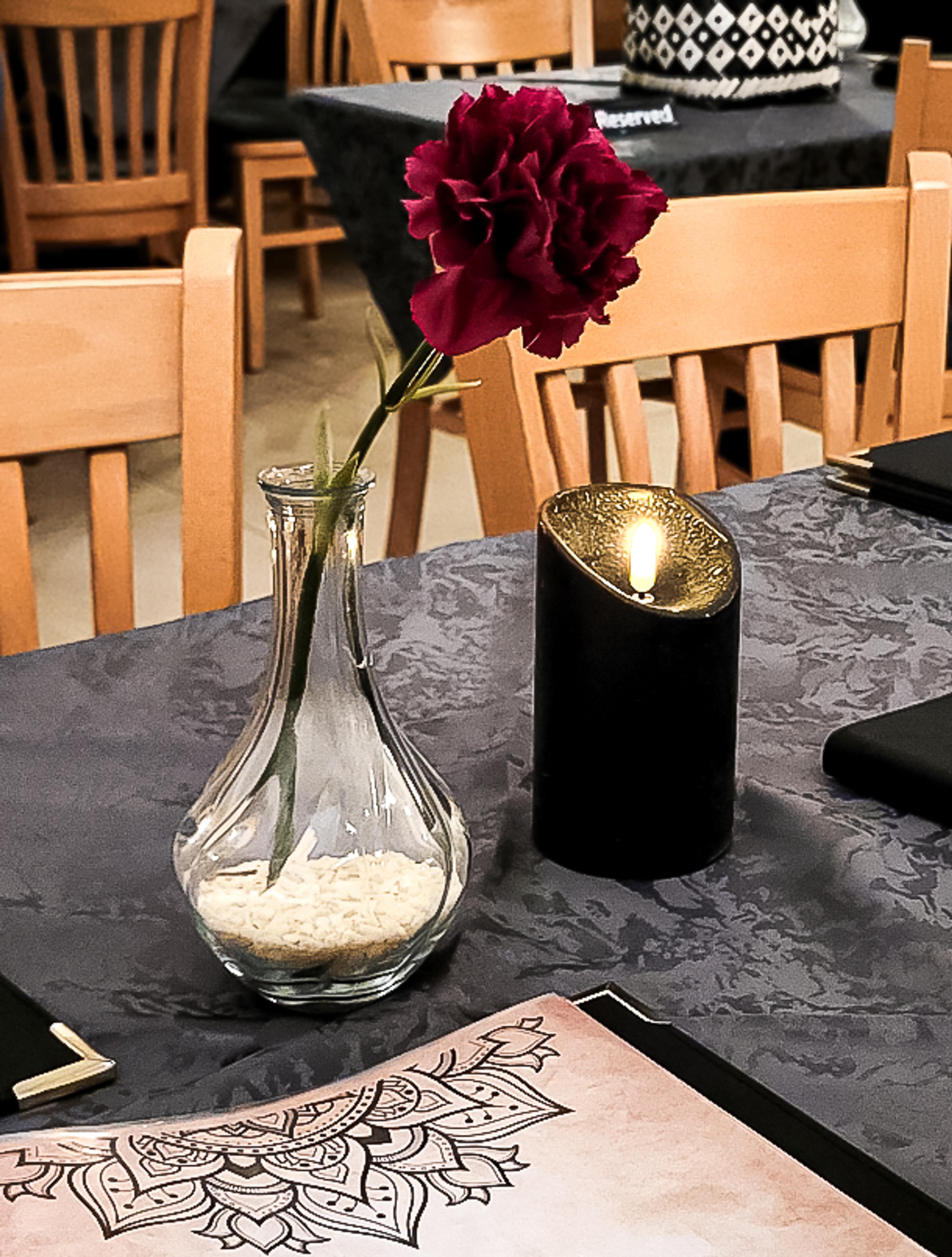 Elegante Tischdekoration im Hathi indischen Restaurant mit einer roten Blume in einer Glasvase und einer stilvollen schwarzen Kerze. Die dunkle Tischdecke mit goldenen Akzenten sorgt für ein luxuriöses Ambiente. Perfekte Interior-Gestaltung für gehobene indische Gastronomie, entwickelt von Unerwartet Branding und Design OG aus Graz, Österreich.