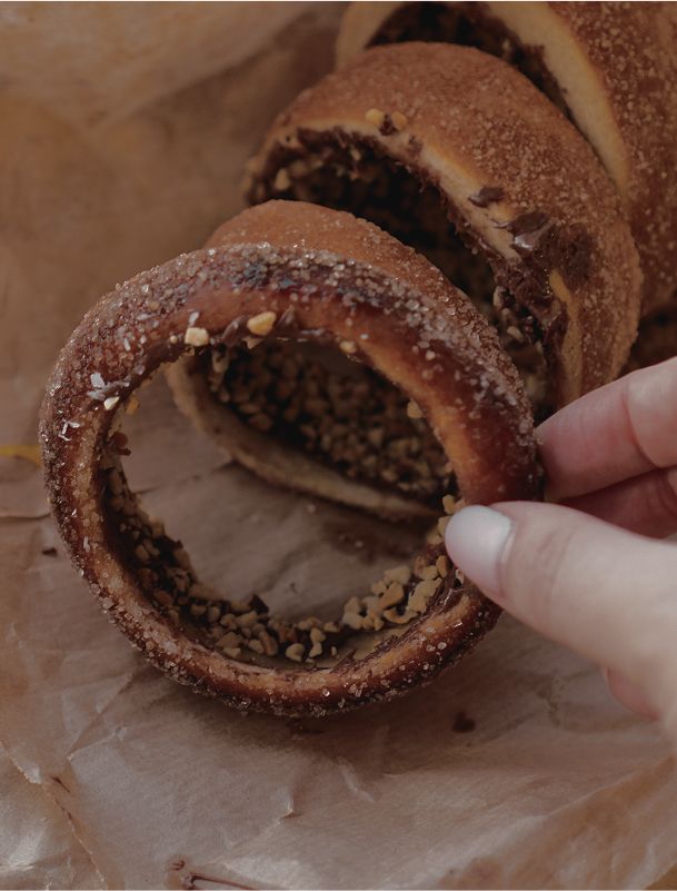 Eine Hand hält einen Baumkuchenring mit Zuckerkruste und gehackten Nüssen.