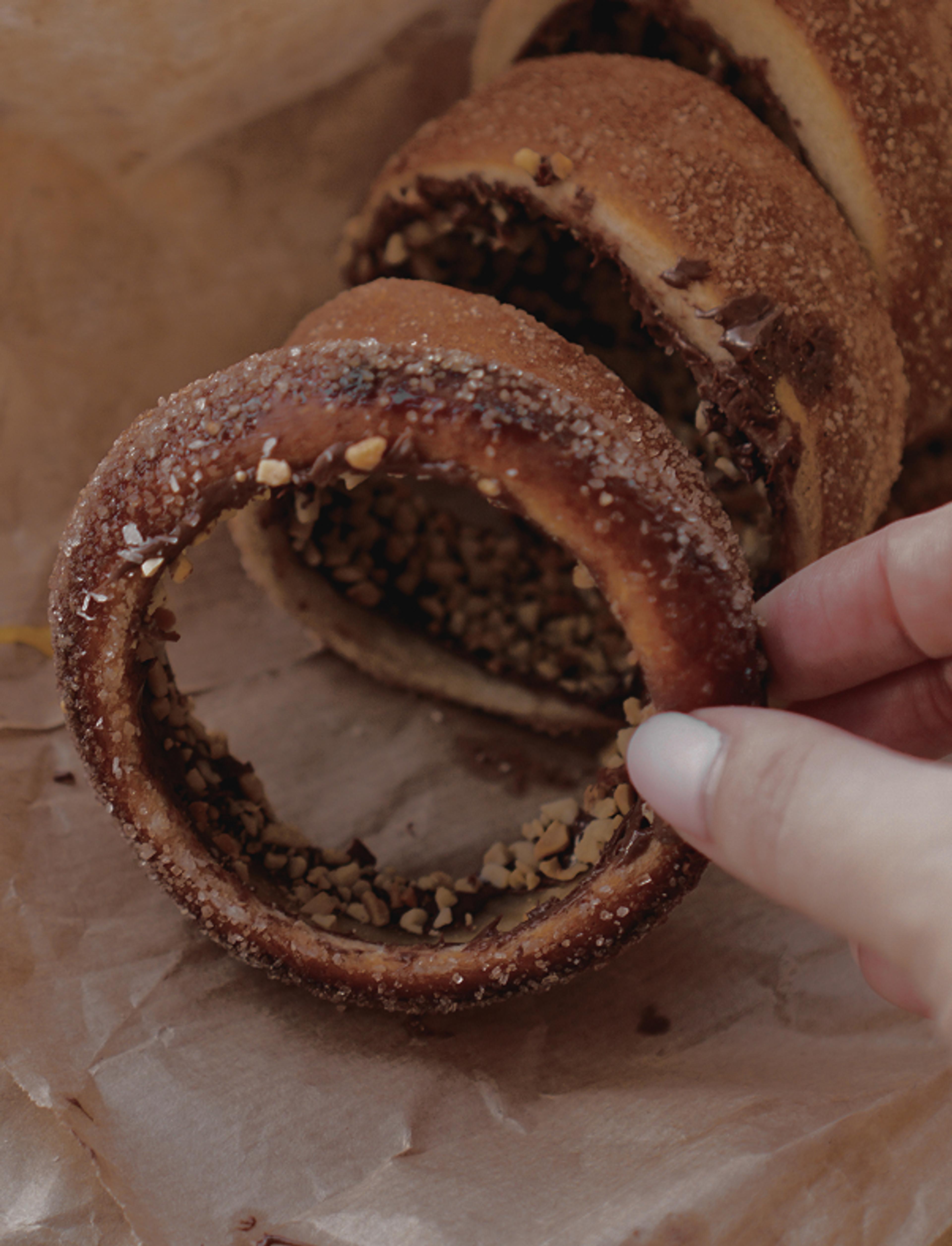 Eine Hand hält einen Baumkuchenring mit Zuckerkruste und gehackten Nüssen.