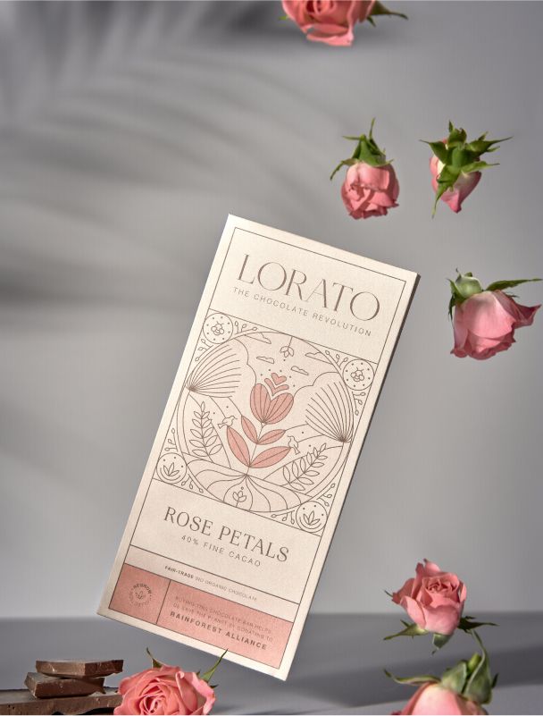 Die Rose Petals Schokoladentafel von Lorato, umgeben von echten Rosenblüten. Elegantes, blumiges Design in sanften Rosétönen.