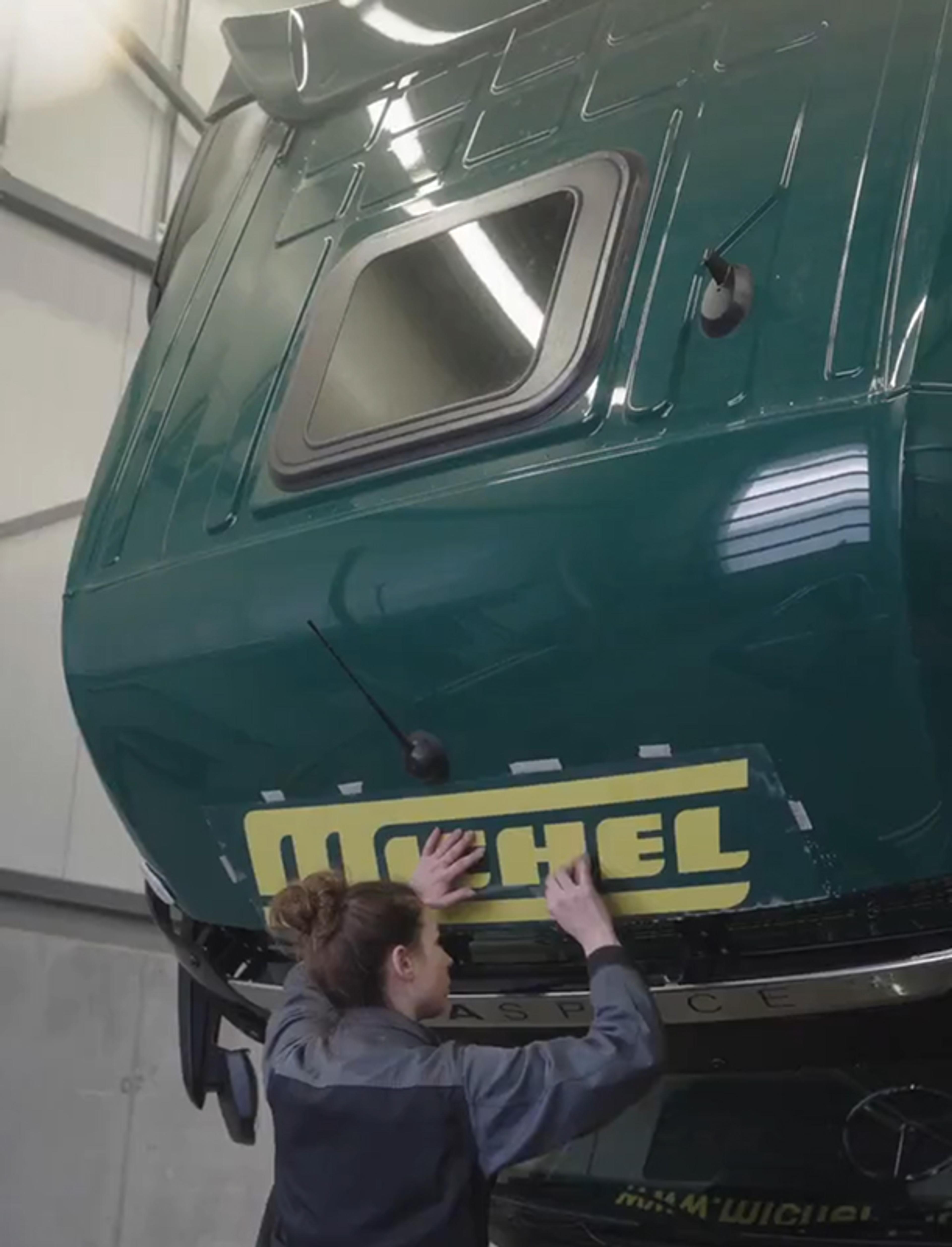 Eine Mitarbeiterin bringt das überarbeitete Michel Logistik Logo auf einem grünen LKW an. Rebranding für Transport- und Logistikmarken von Unerwartet Design.