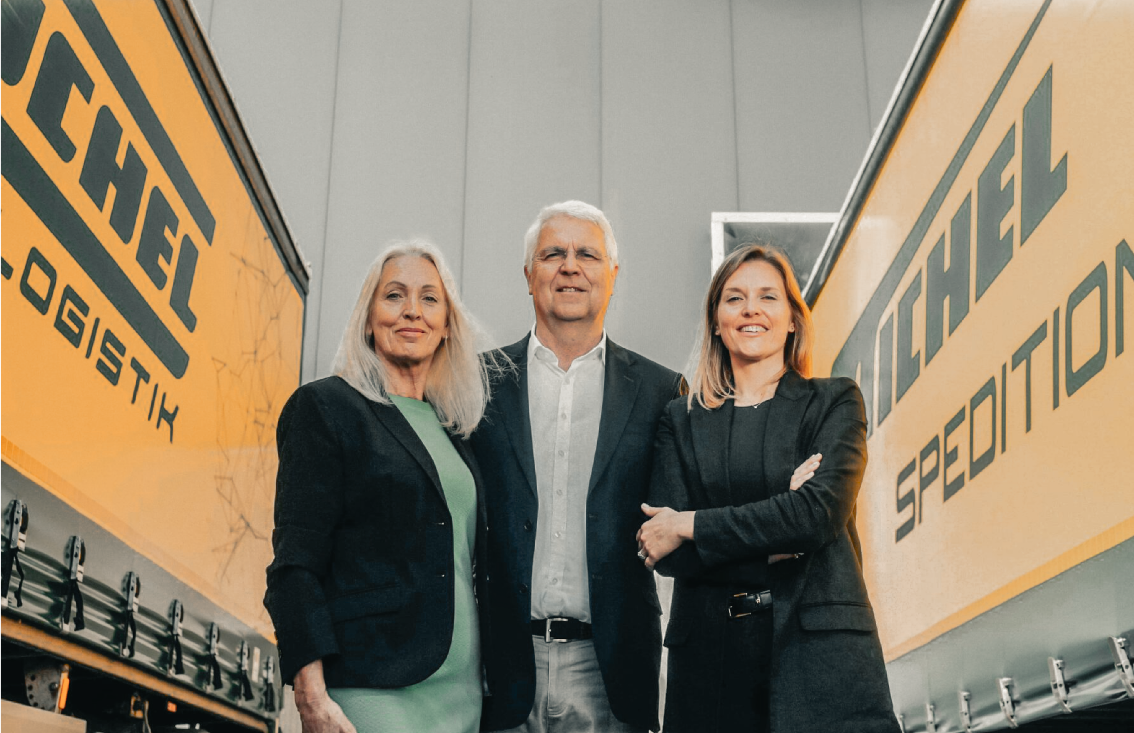 Geschäftsführung von Michel Logistik zwischen zwei LKWs, fotografiert in einer professionellen Umgebung – Rebranding von Unerwartet Design.