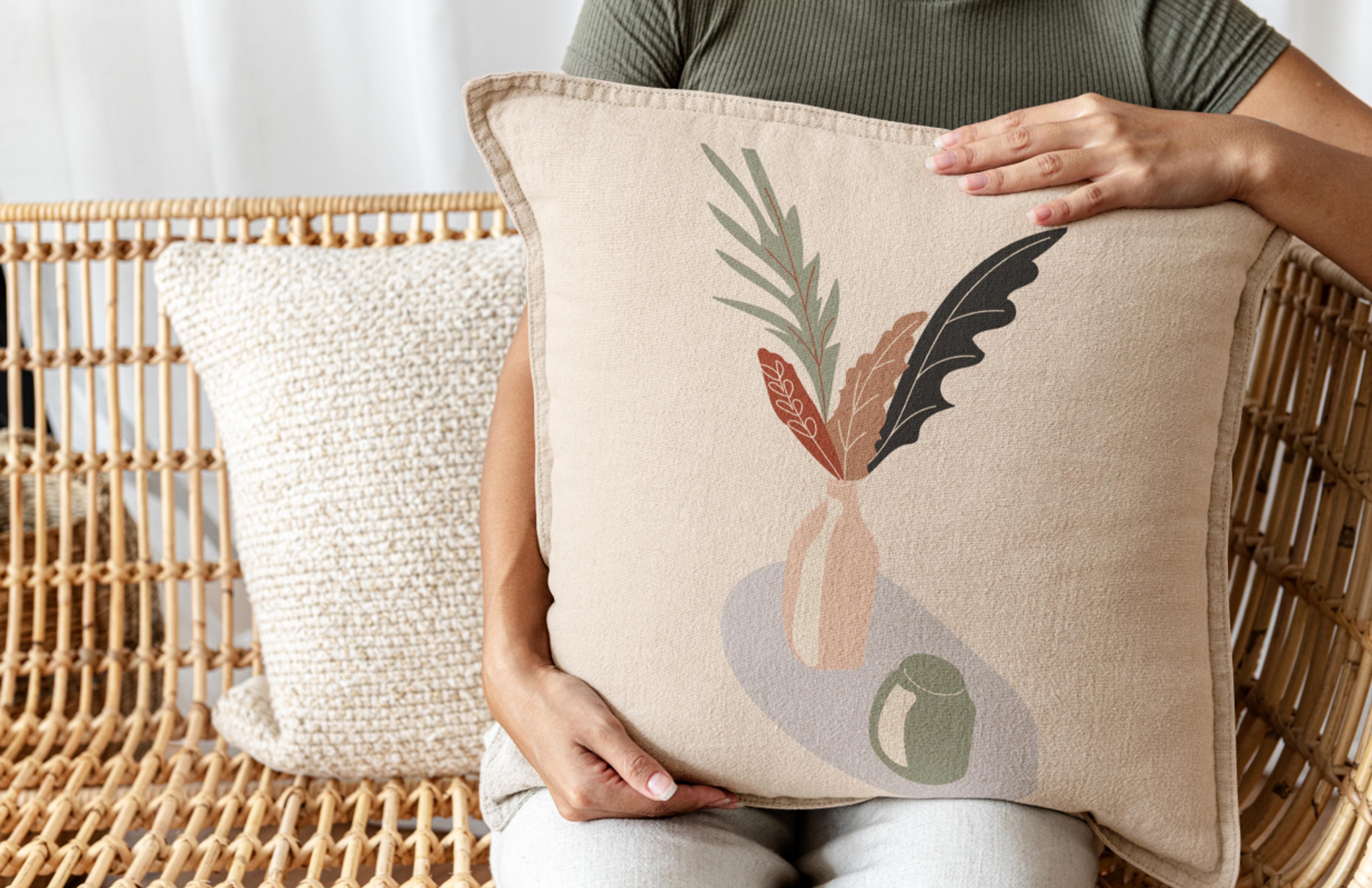 Kissen mit Pflanzenillustration und natürlicher Rattansessel im modernen Wohndesign, nachhaltiges Branding von Rattatat durch Unerwartet Design.