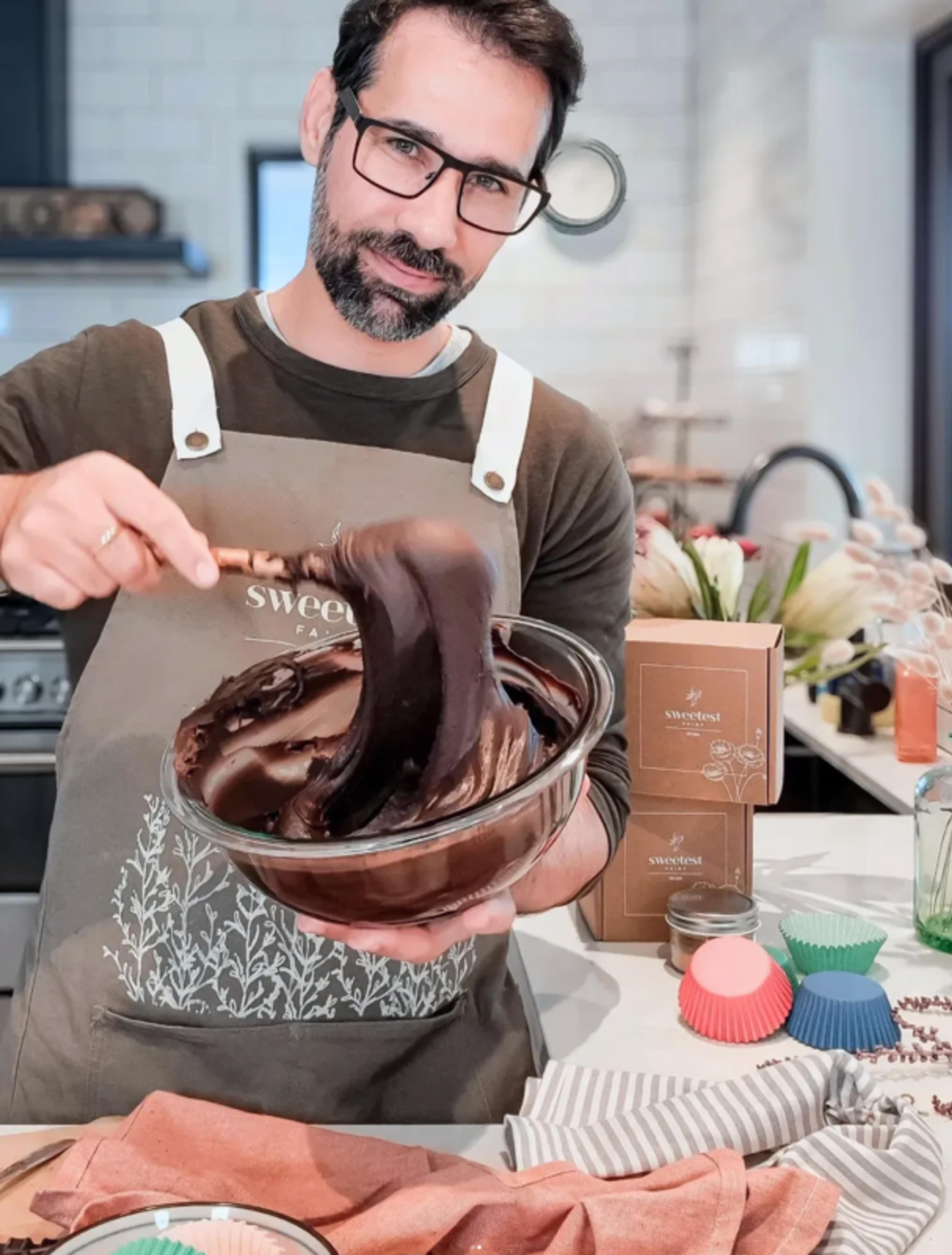 Sweetest Fairy | Sarah Frost Ein Bäcker in einer stilvollen Küche rührt eine reichhaltige, cremige Schokoladenmasse in einer Glasschüssel. Im Hintergrund luxuriöse Geschenkverpackungen und nachhaltige Branding-Elemente für exklusive Feinkostprodukte. Perfektes Verpackungsdesign für hochwertige Patisserien, Schokoladenmarken und Premium-Geschenkverpackungen. Branding und Design von Unerwartet Branding und Design OG aus Graz, Österreich.