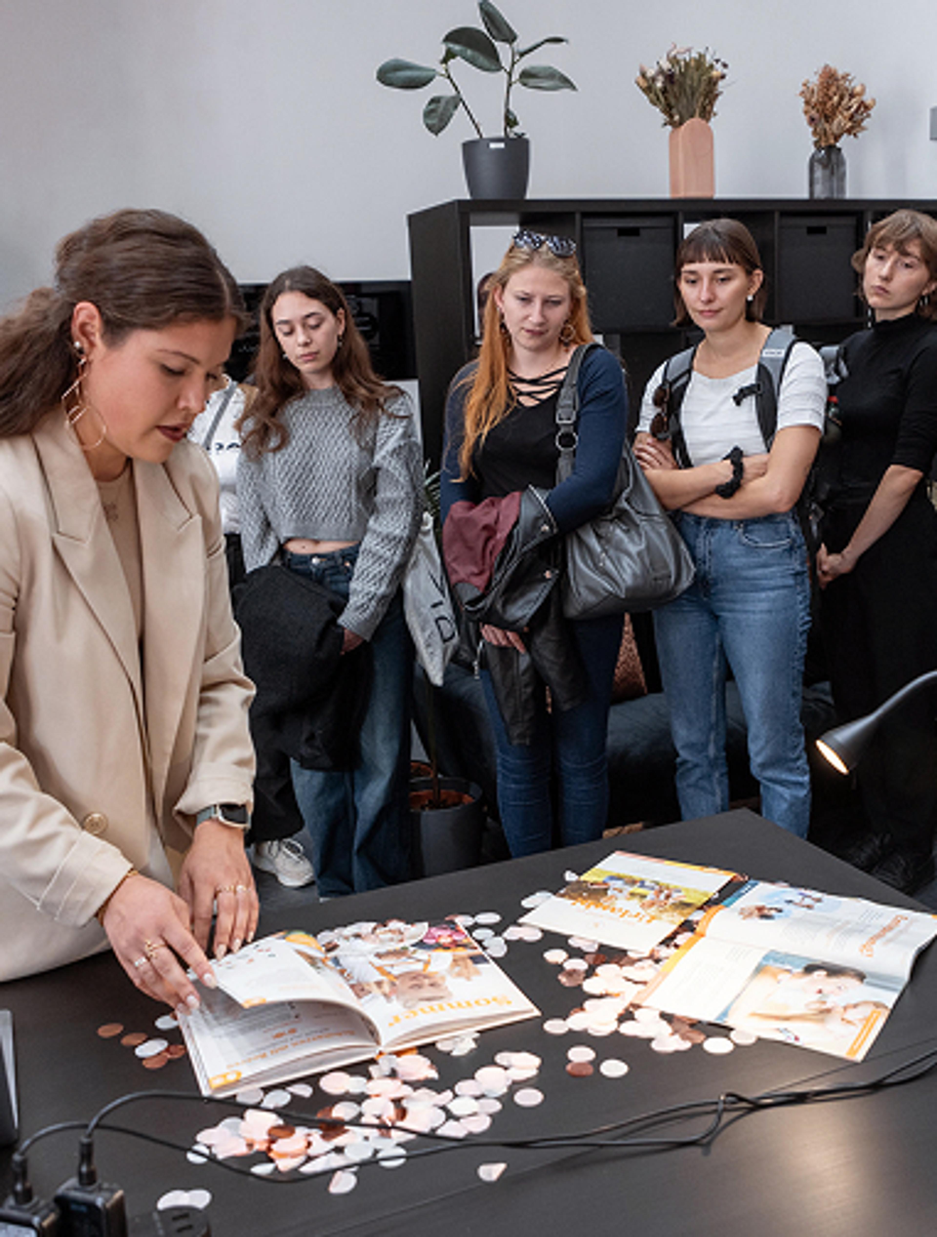Valerie Zengerer zeigt unsere Projekte vor einem großem Publikum, während der Creative Night 2023. Ausstellung in Unerwartet Design Büro in der Belgiergasse 16, im Herzen von Graz. Studentinnen aus der FH Joanneum, Studiengang Informationsdesign schauen zu. Eine Initiative der Creative Industries Styria.