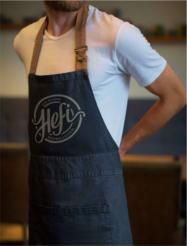 Ein Mitarbeiter trägt eine dunkelgraue Schürze mit dem Hefi-Logo in einem Café.
