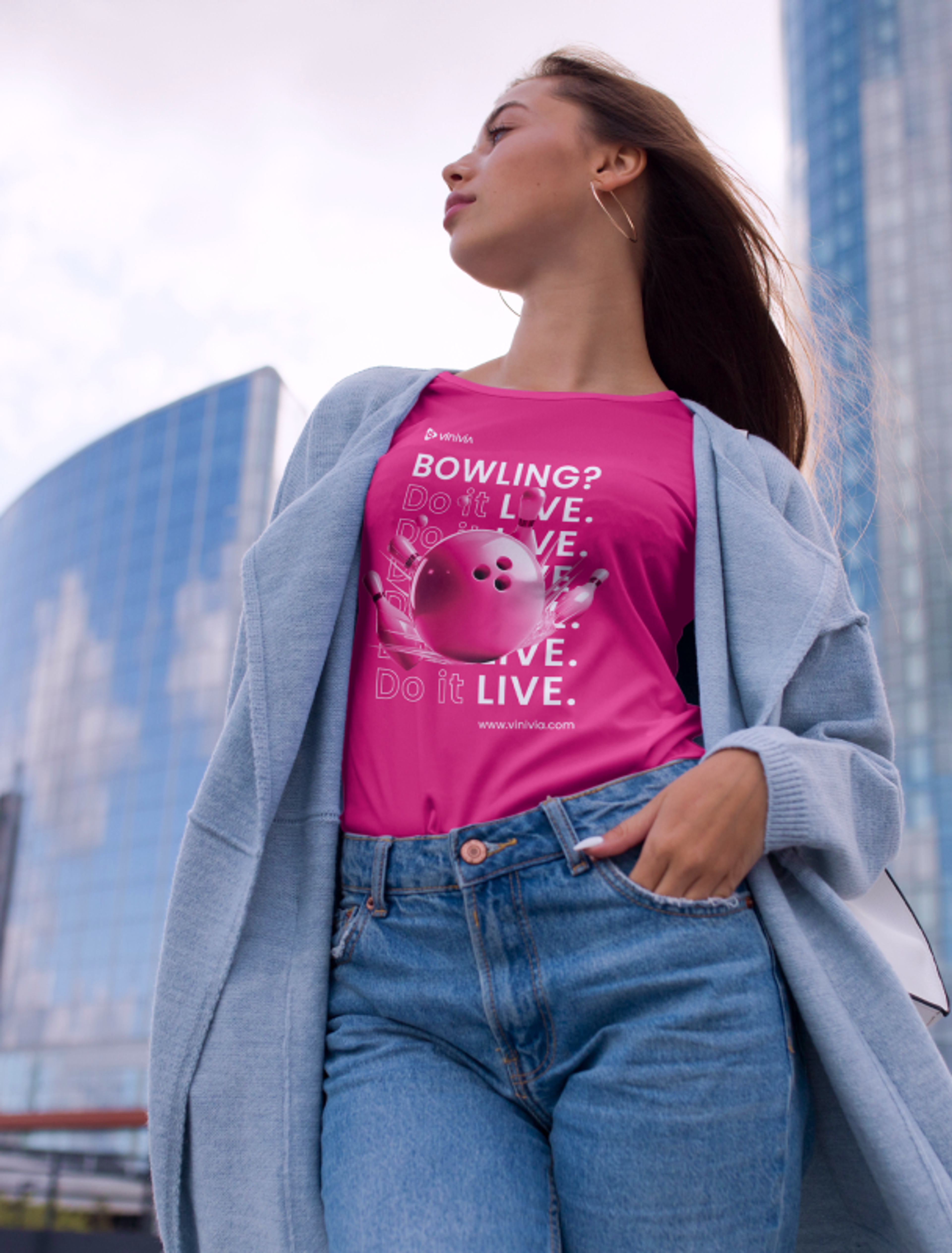 Frau in pinkem Vinivia-T-Shirt "Bowling? Do it LIVE." vor moderner Stadtlandschaft, stilvolles Design für aktive Zielgruppen - Unerwartet Design.