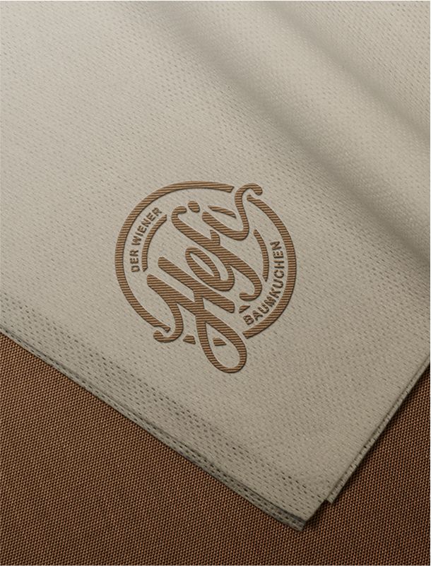 Eine beige Stoffserviette mit eingeprägtem Hefi-Logo auf braunem Untergrund.