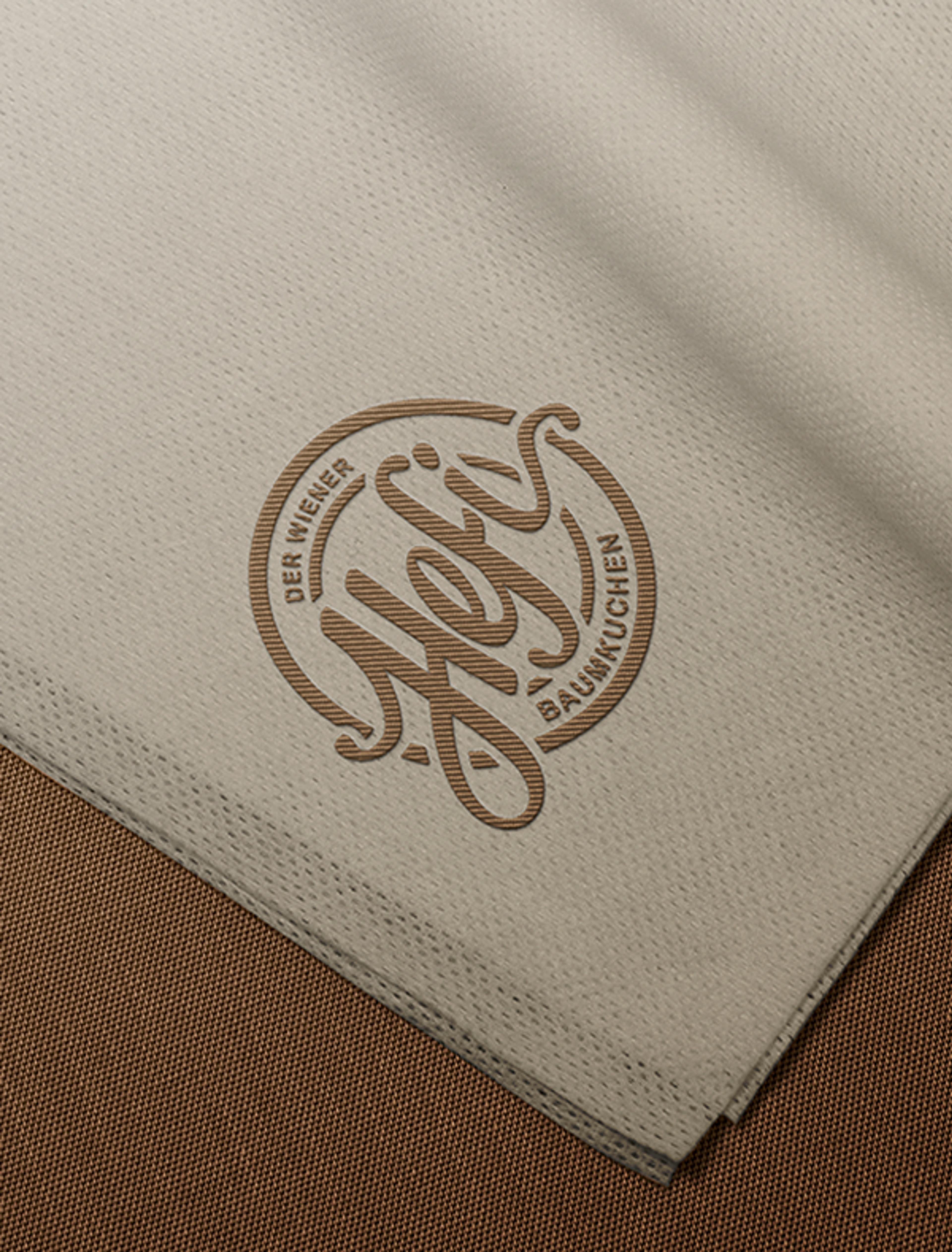 Eine beige Stoffserviette mit eingeprägtem Hefi-Logo auf braunem Untergrund.