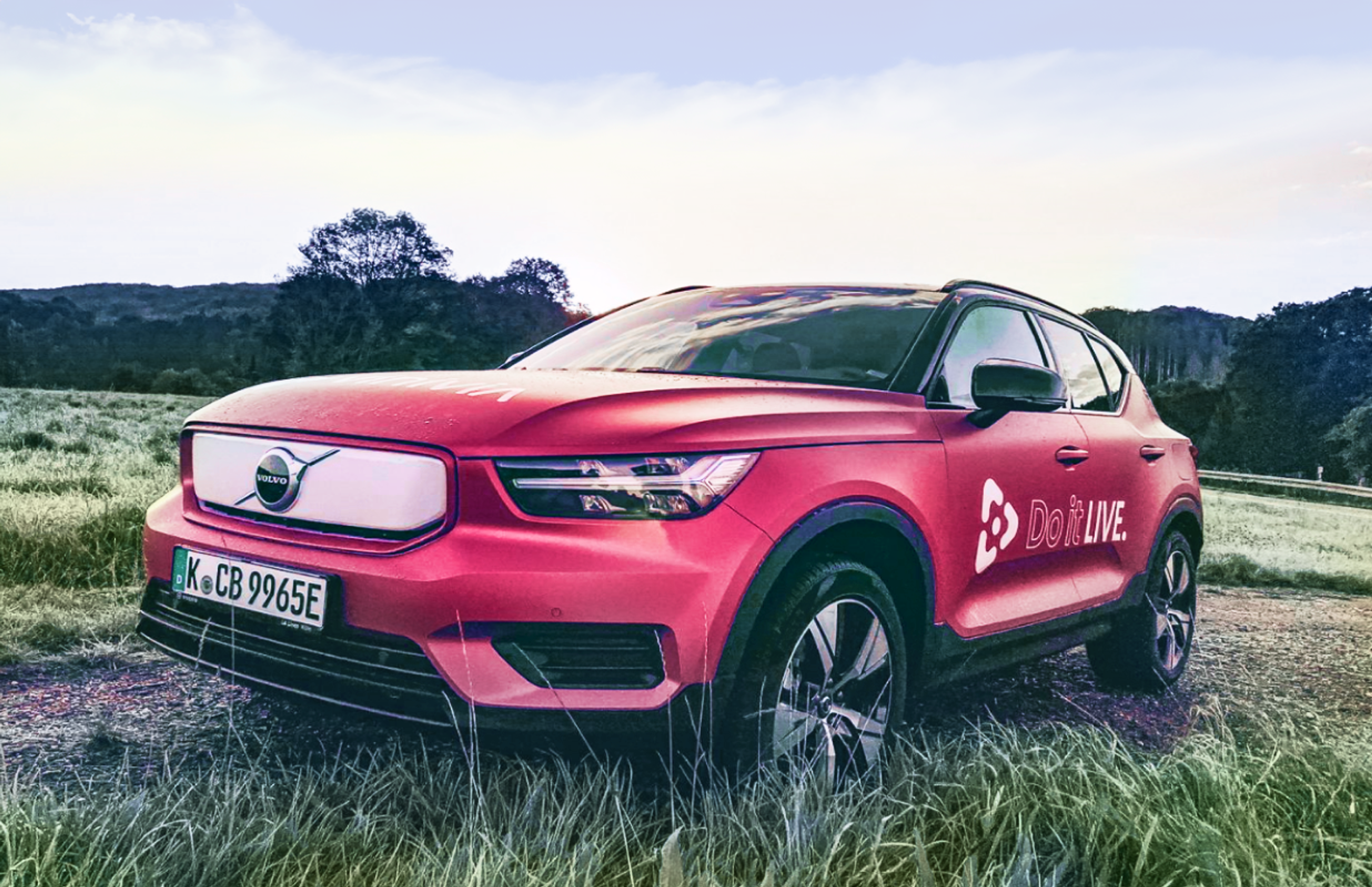 vinivia Elektro-SUV im Vinivia-Branding, platziert in einer idyllischen Naturlandschaft bei Sonnenuntergang, mit auffälligen Markenfarben - Unerwartet Design