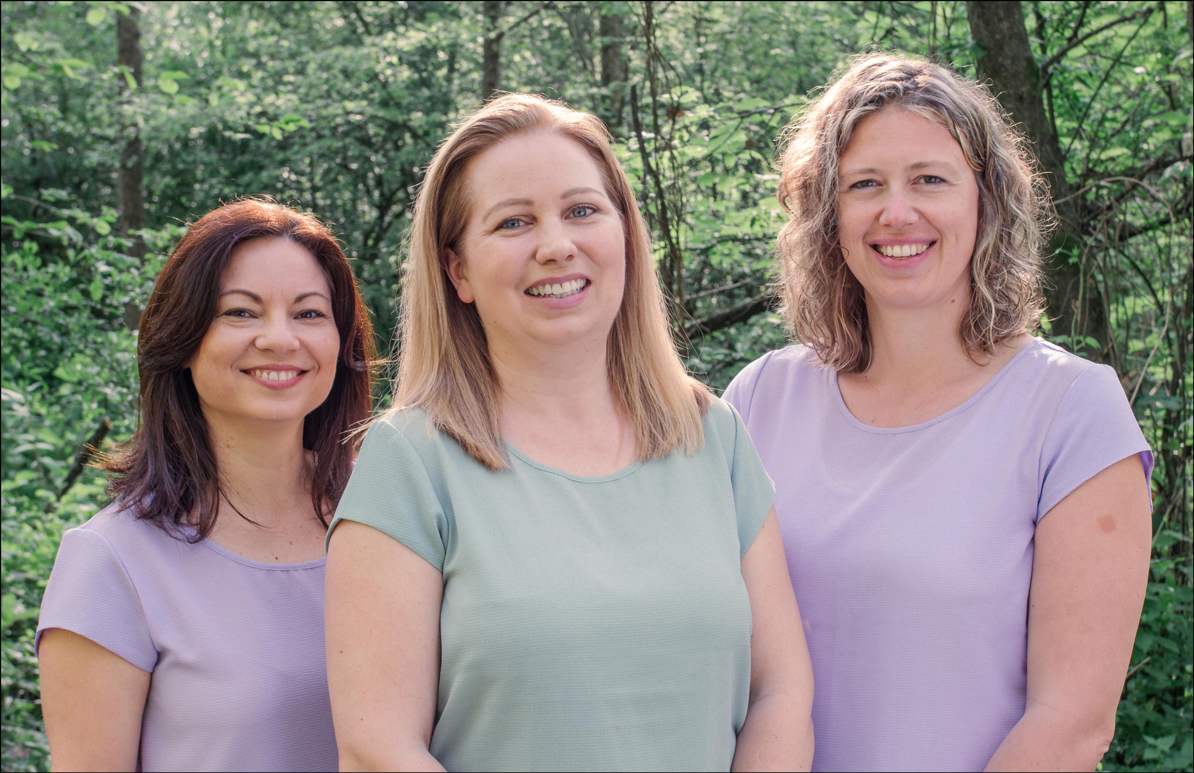 Teamfoto von Mag. Bernadette Becke, Viola Grassler und Dr. Gerhild Weiß, aufgenommen im Grünen vom Ijob Brandstätter, mit Branding-Elementen von Unerwartet Design Graz.