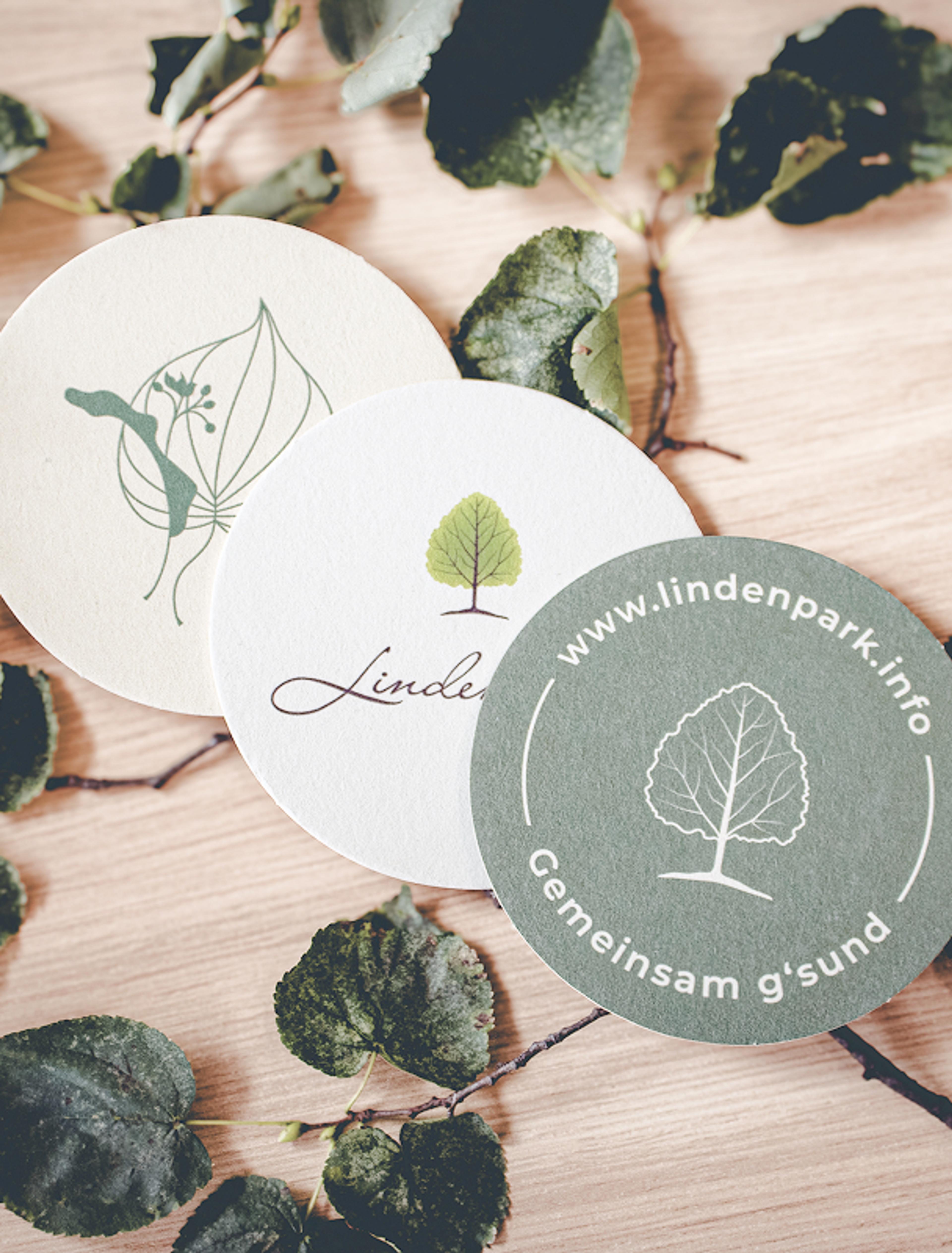 Logo & Grundkonzept BUCHER BRAND MARKETING e.U. Runde Bierdeckel mit Lindenpark-Logo und Baum-Motiv in Grün und Weiß, gestaltet von Unerwartet Design.