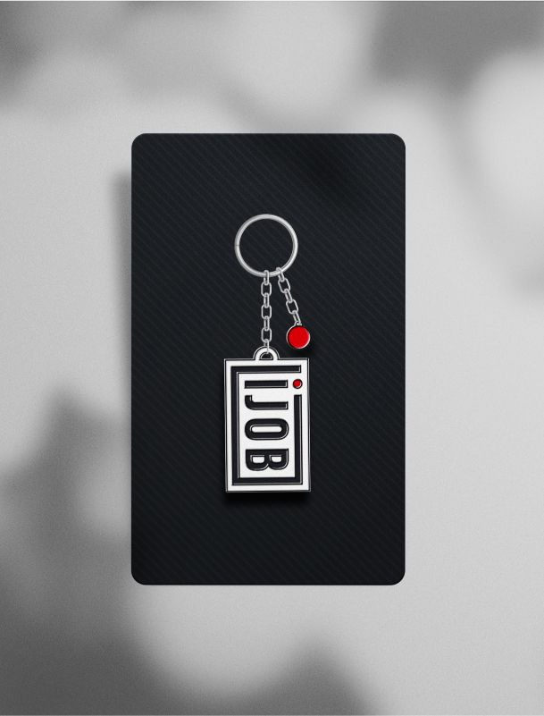 Ein silberner Schlüsselanhänger mit dem Ijob-Logo, befestigt an einer Metallkette. Das Design kombiniert Schwarz, Weiß und Rot, passend zur Markenidentität.