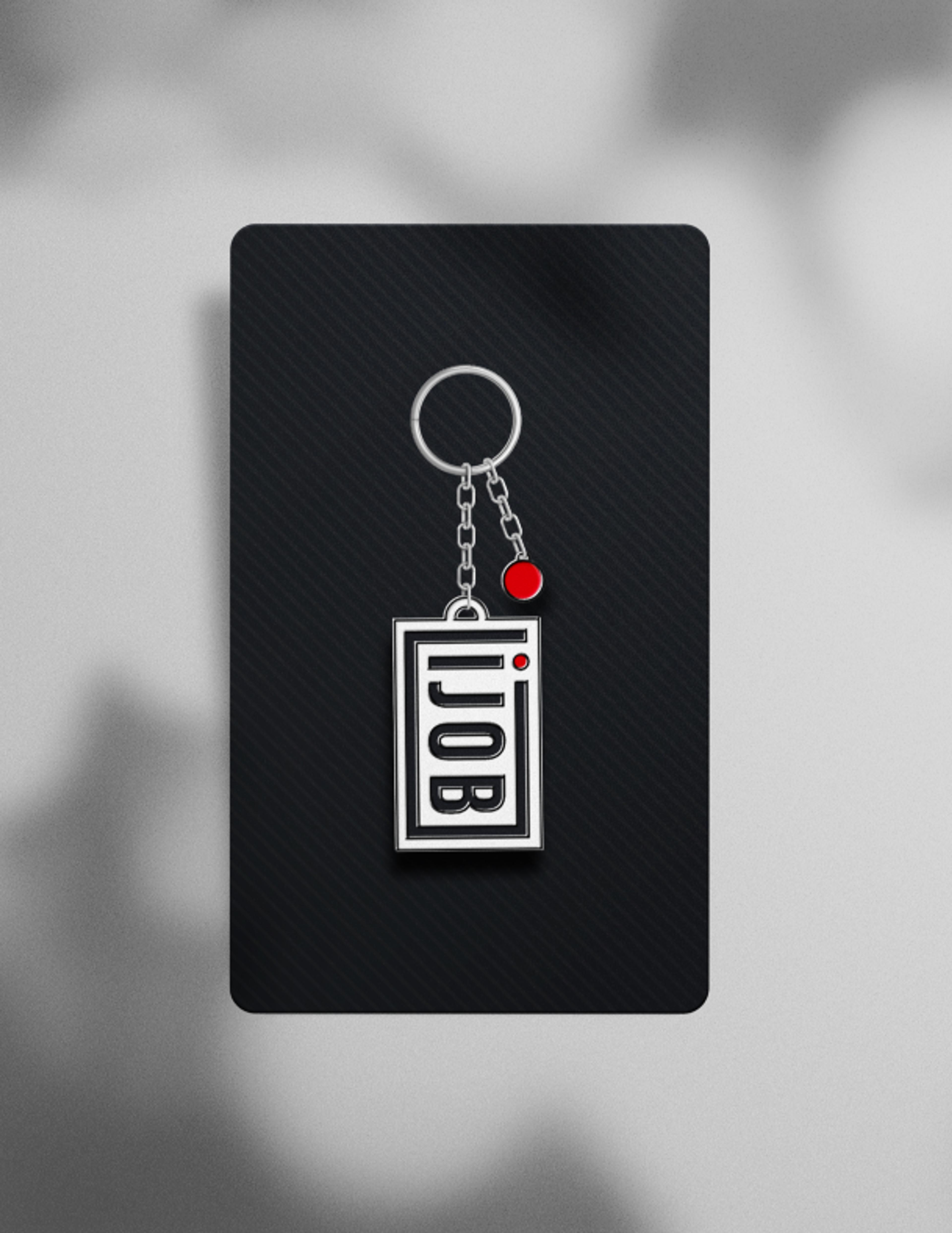 Ein silberner Schlüsselanhänger mit dem Ijob-Logo, befestigt an einer Metallkette. Das Design kombiniert Schwarz, Weiß und Rot, passend zur Markenidentität.