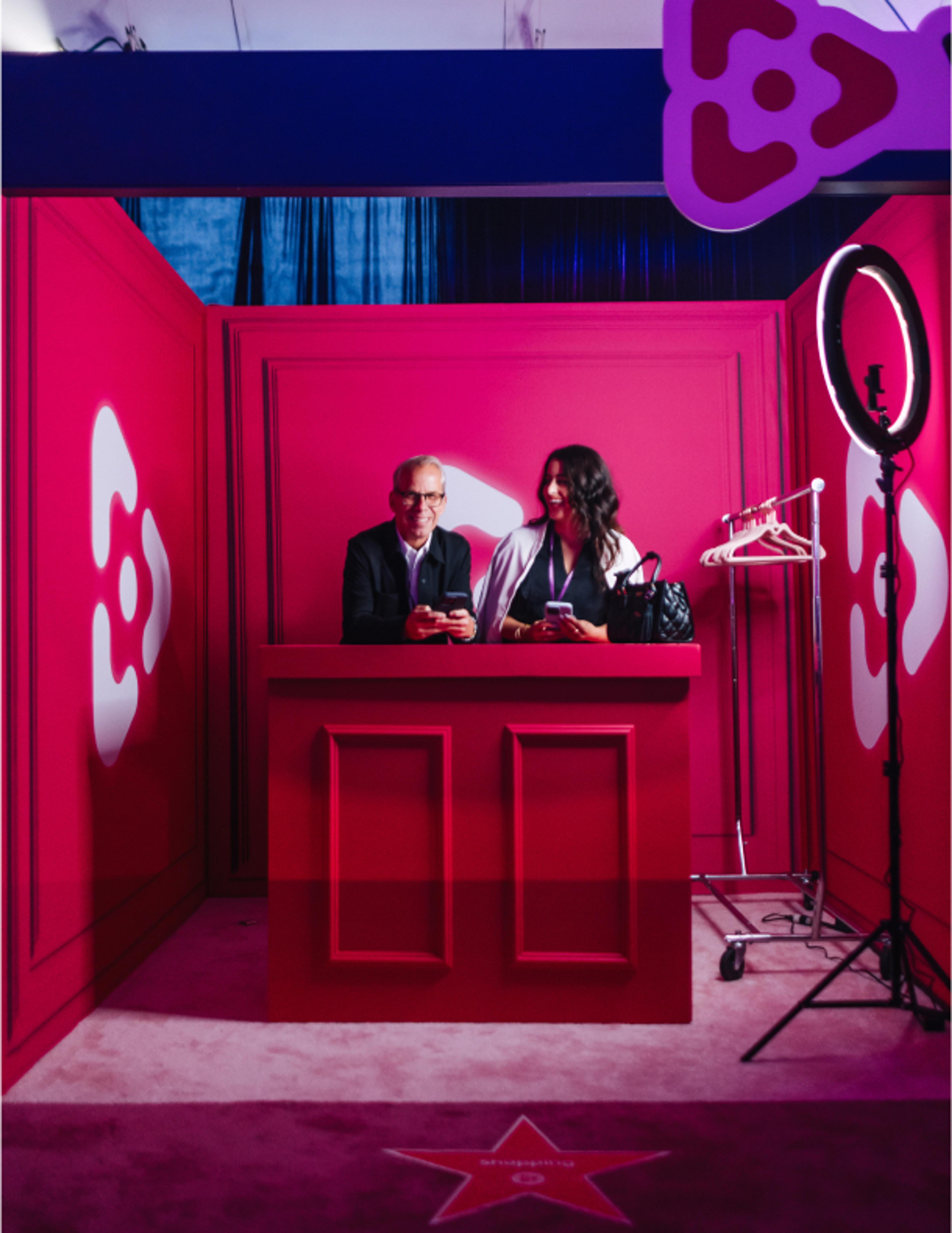 Foto: vinivia, bfa, jorgemezaphotos Vinivia Lounge mit Interview-Setup: Tisch, Mikrofone und beleuchtete Logos in pinkem Event-Design – Unerwartet Design