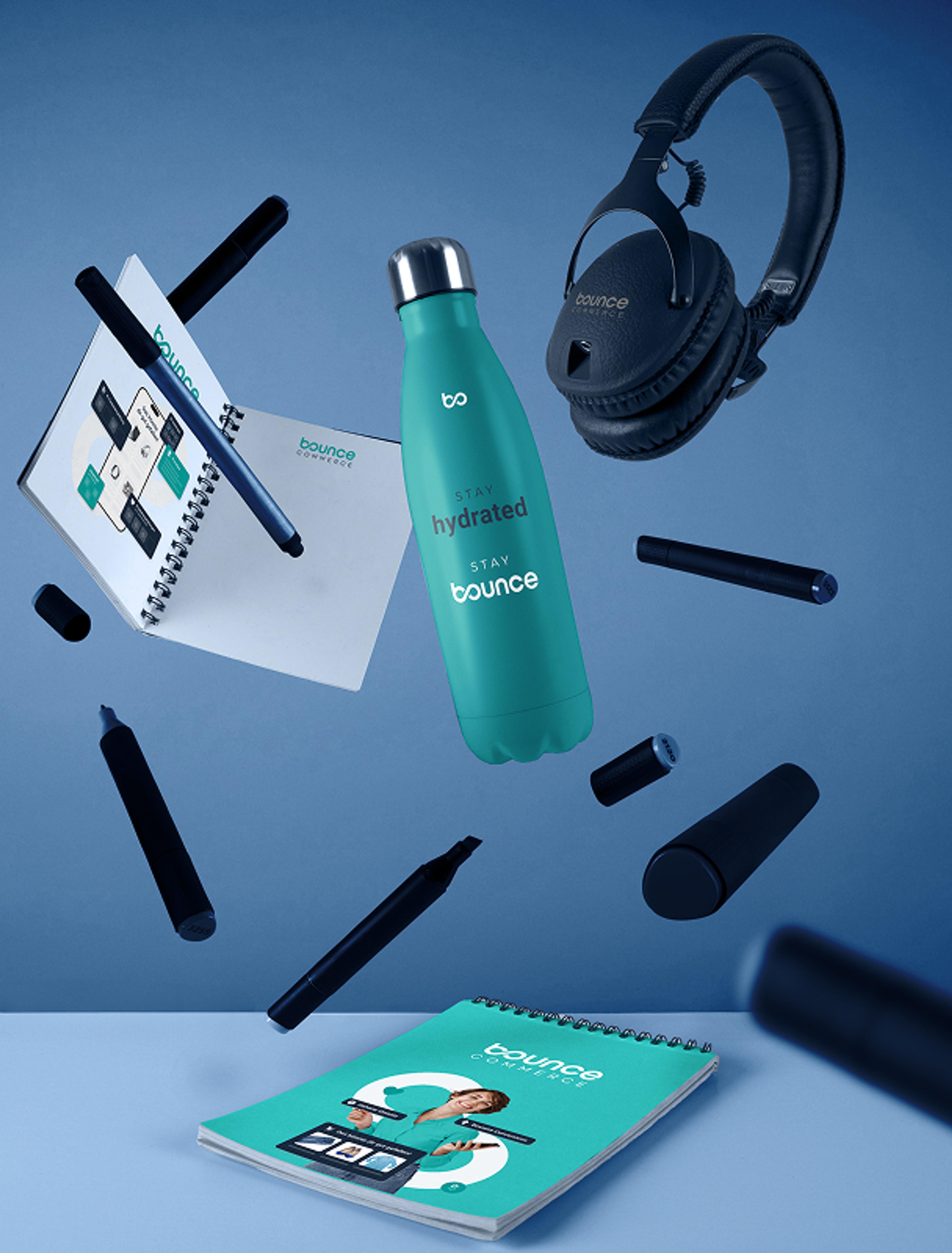 3D-Visualisierung von Marken-Merchandise für Bounce Commerce, inklusive gebrandeter Flasche, Notizbuch und Kopfhörer in moderner Ästhetik.