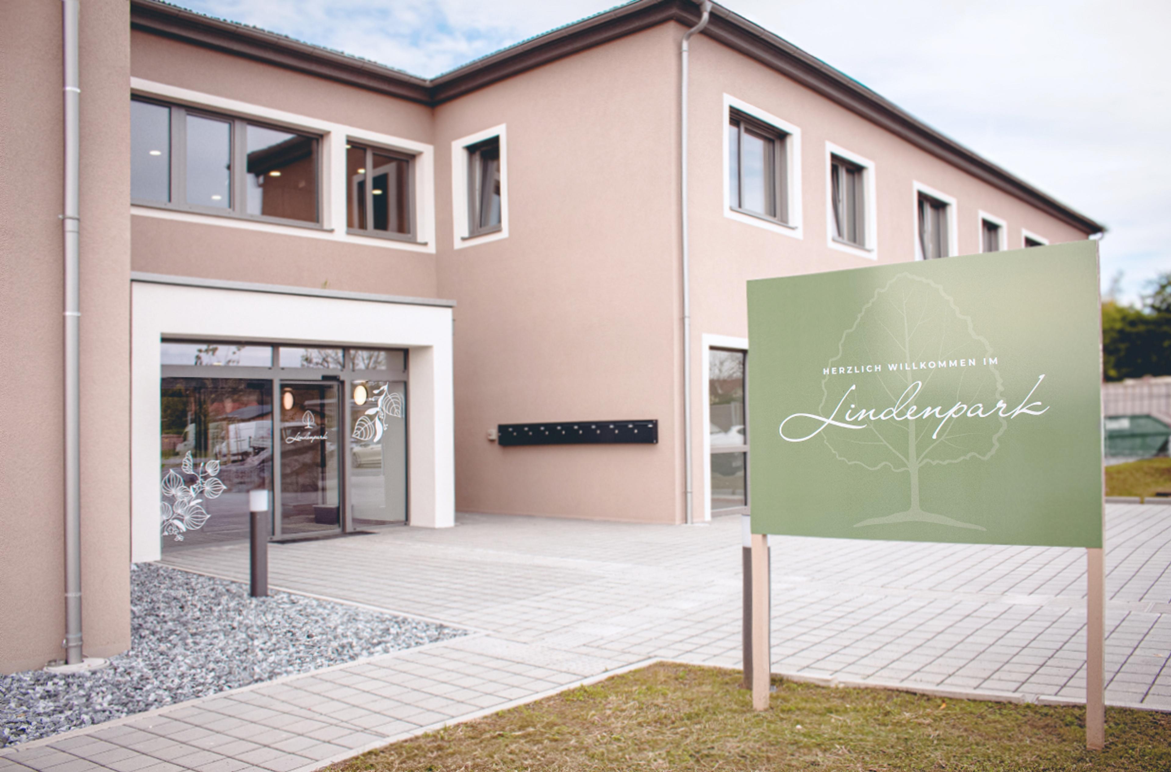 Logo & Grundkonzept BUCHER BRAND MARKETING e.U. Außenansicht des Lindenpark Gesundheitszentrums in Gössendorf mit harmonisch gestaltetem Schild "Herzlich Willkommen im Lindenpark", Teil des Branding- und Designkonzepts von Unerwartet Design.