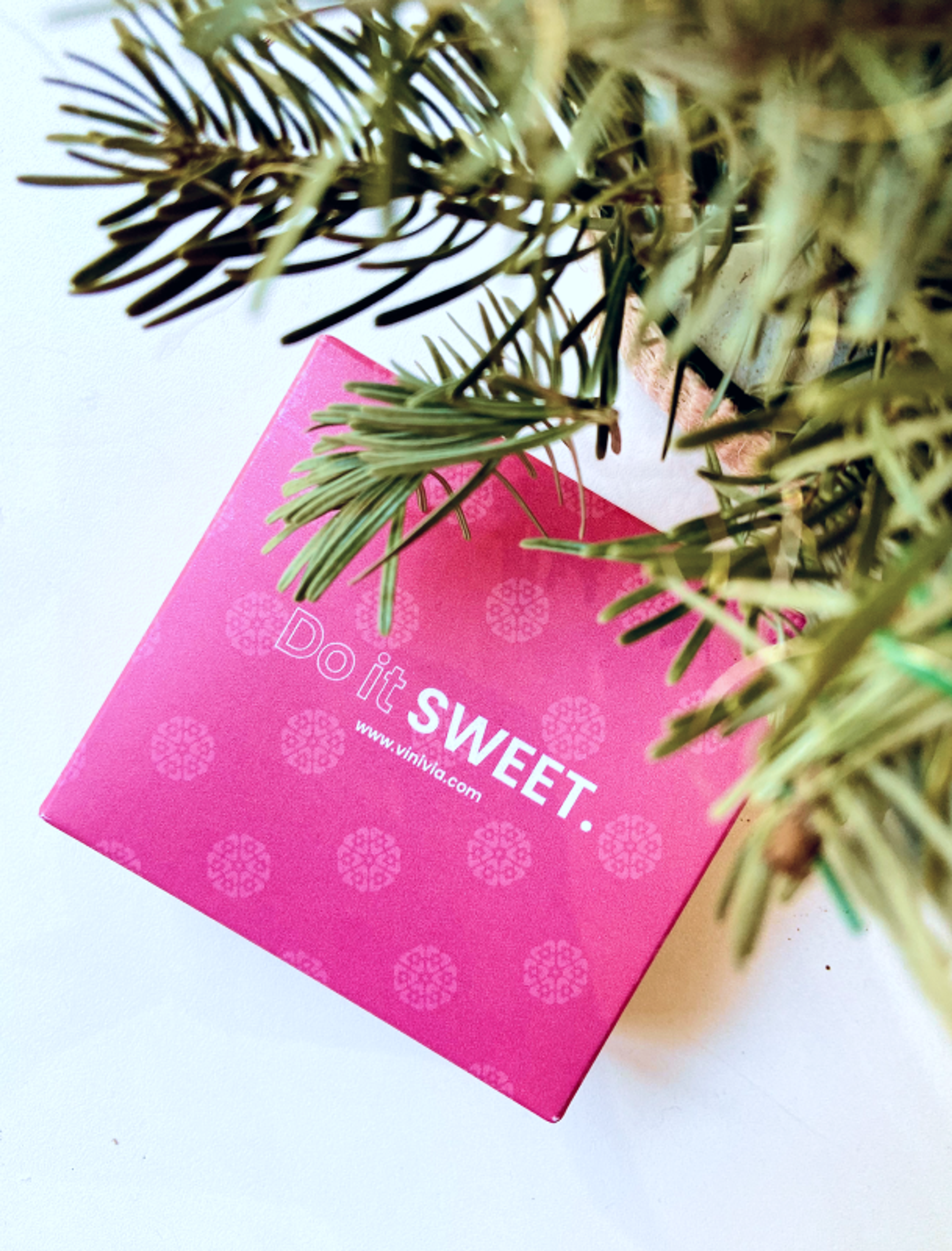 Pinke Vinivia-Geschenkbox mit der Aufschrift "Do it SWEET" unter einem weihnachtlichen Tannenbaum, passend zur festlichen Weihnachtskollektion – Unerwartet Design