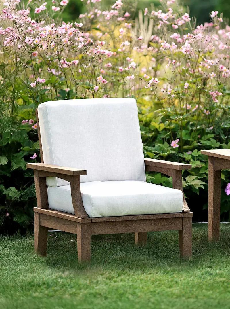 Outdoor lounge chair with white cushions and wooden frame placed in garden with flowers.