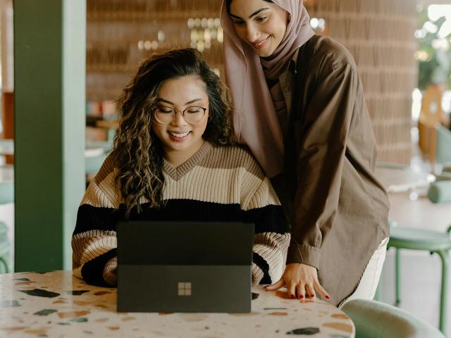 two women are sitting at a table looking at a laptop