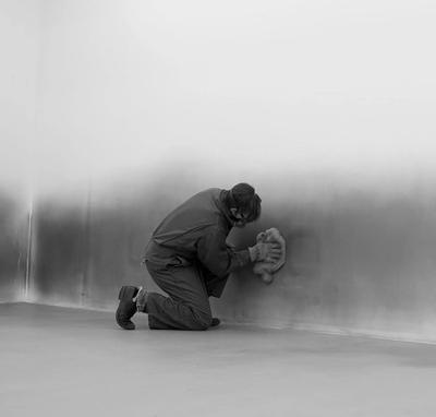 man rubbing black residue on gallery wall