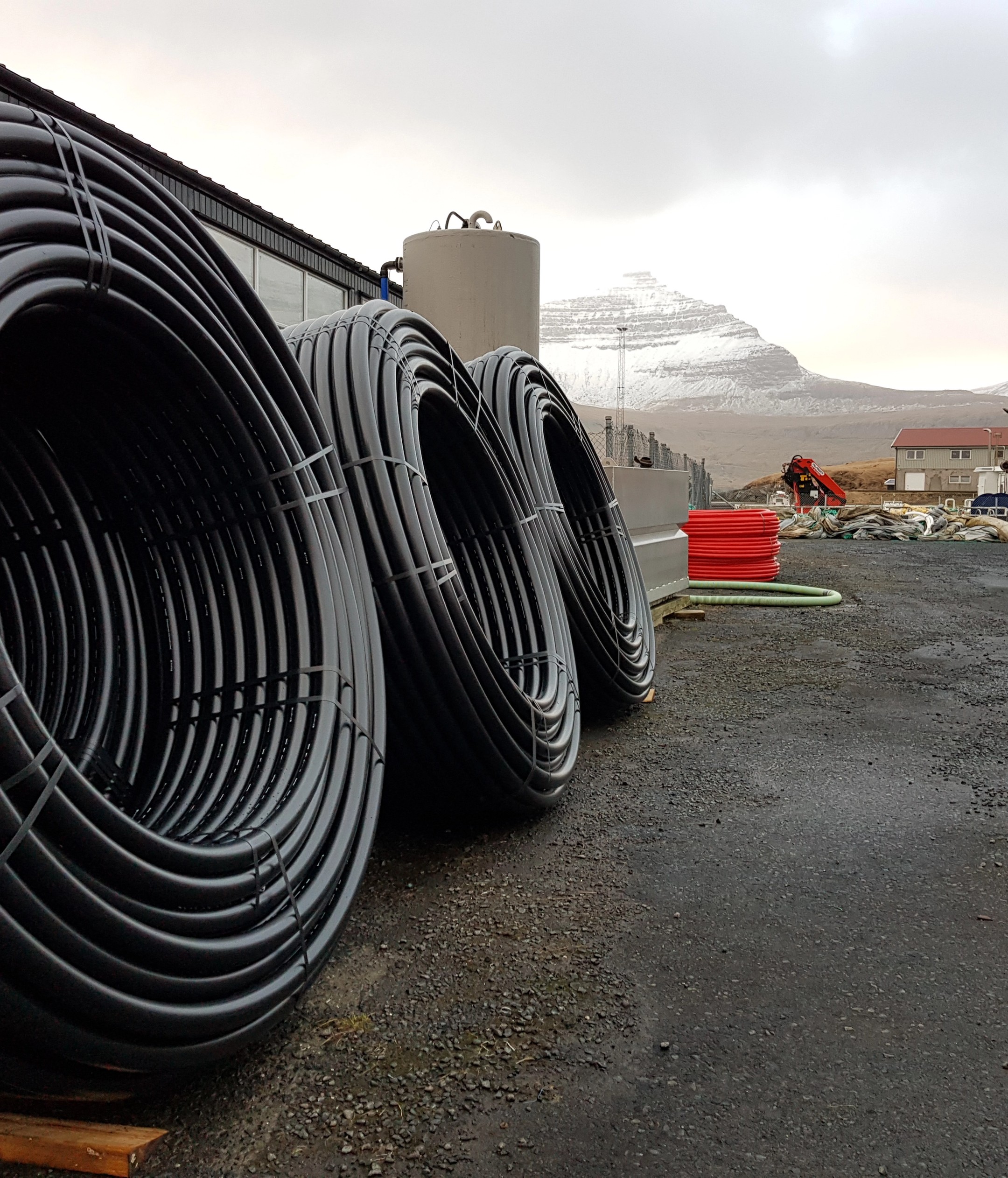 Coiled black HDPE pipes stored outdoors at an aquaculture service facility, ready for use in pen and feed systems.