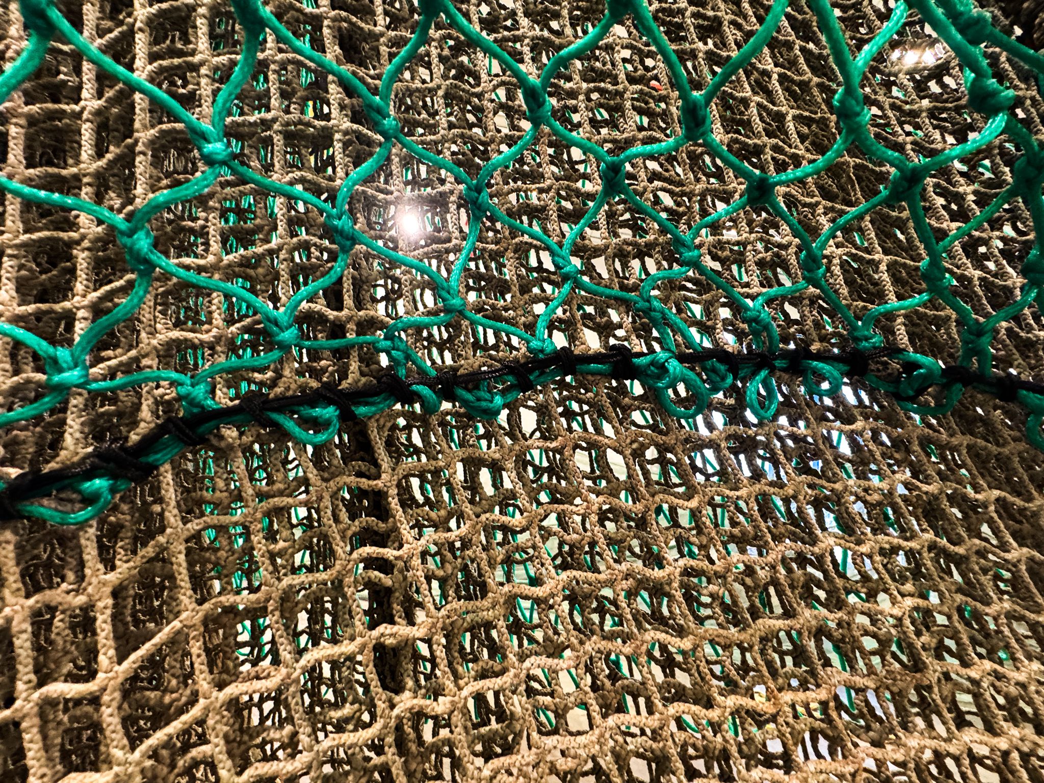 Close-up of reinforced aquaculture predator netting with thick, knotted rope construction, designed to withstand abrasion and gnawing from predators at the bottom of fish cages.