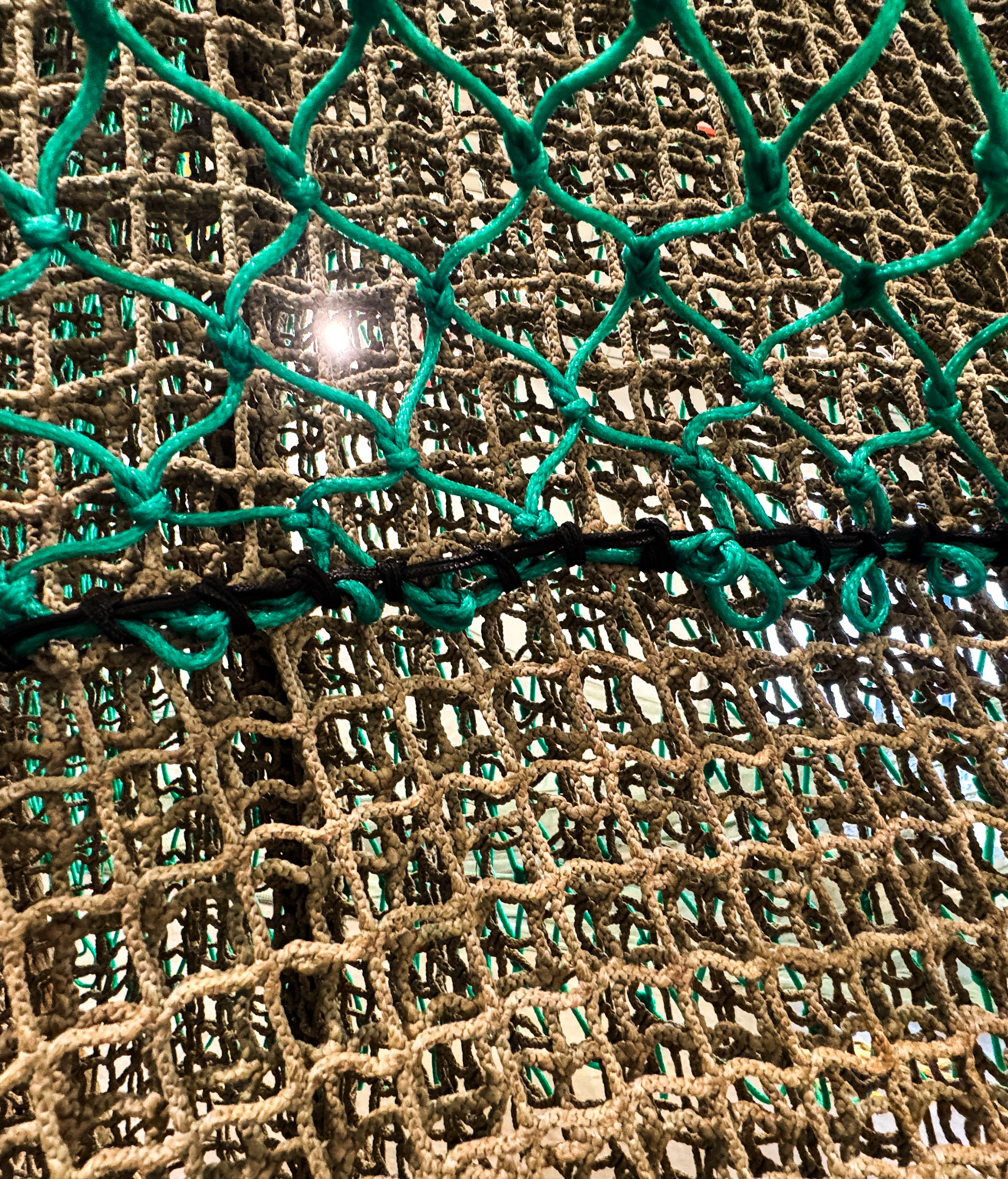 Close-up of reinforced aquaculture predator netting with thick, knotted rope construction, designed to withstand abrasion and gnawing from predators at the bottom of fish cages.