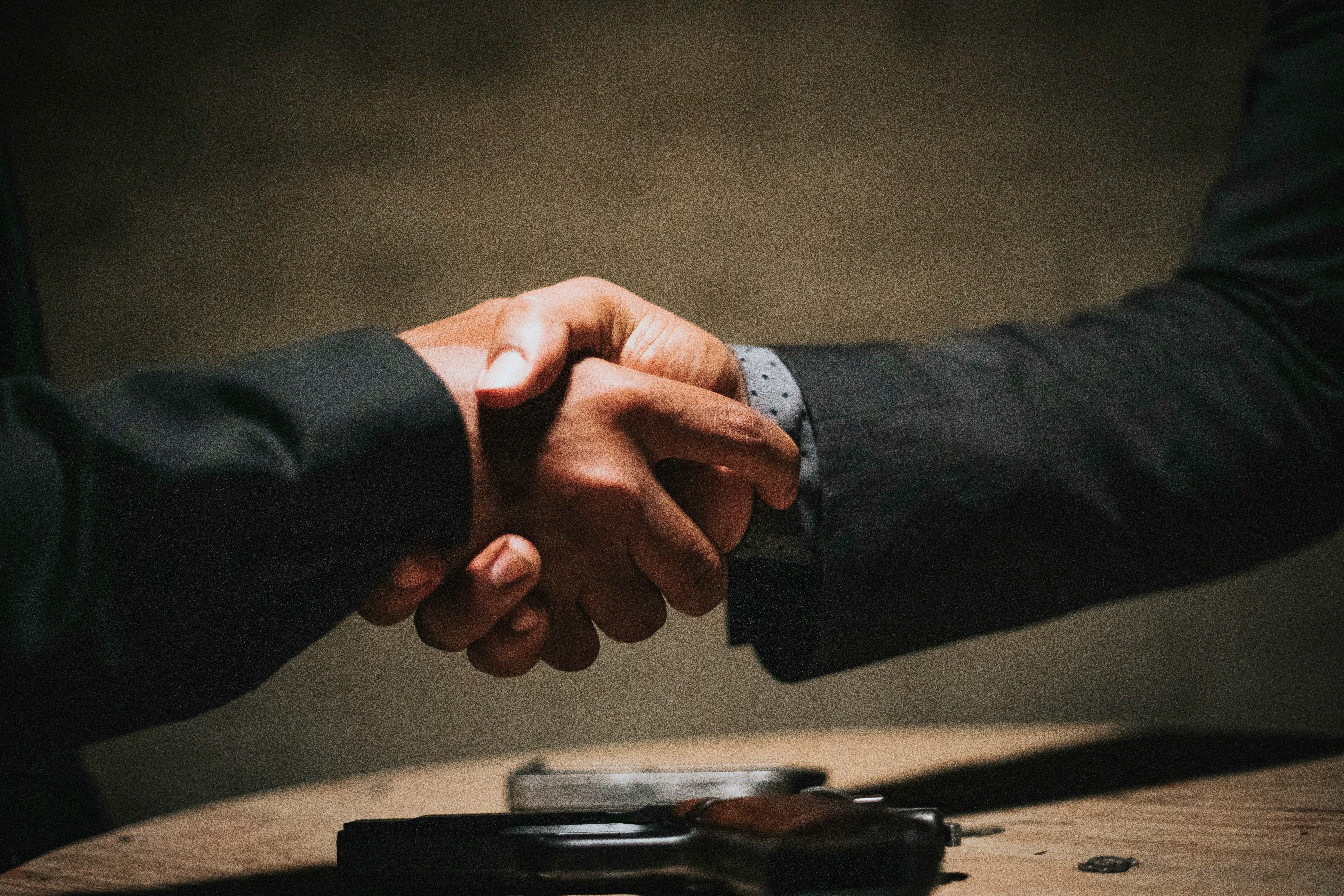 Business handshake across a desk, illustrating the trust relationships that leaders can either build or destroy through their management approach