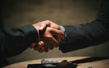 Business handshake across a desk, illustrating the trust relationships that leaders can either build or destroy through their management approach