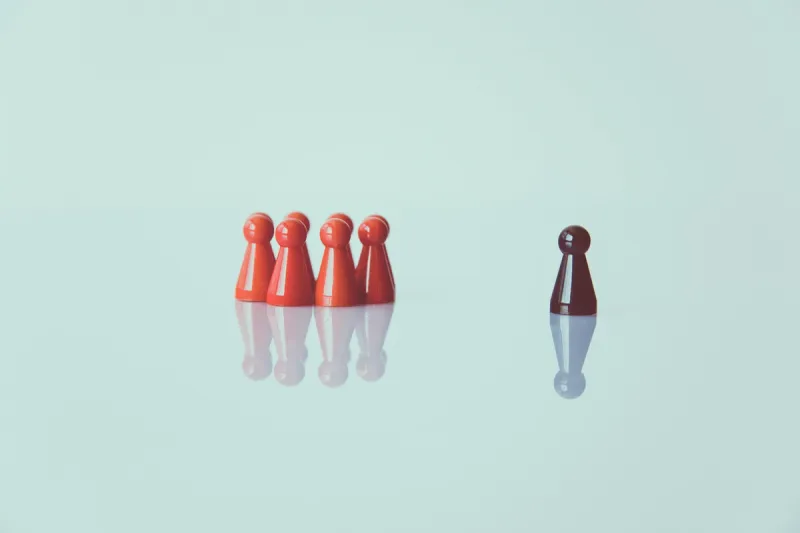 A lone dark game piece standing apart from a group of red pieces, illustrating leadership independence and confidence
