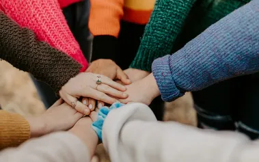 Multiple hands in joining together in a team gesture, illustrating the unity and belonging that comes from inclusive culture beyond diverse hiring