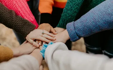 Multiple hands in joining together in a team gesture, illustrating the unity and belonging that comes from inclusive culture beyond diverse hiring